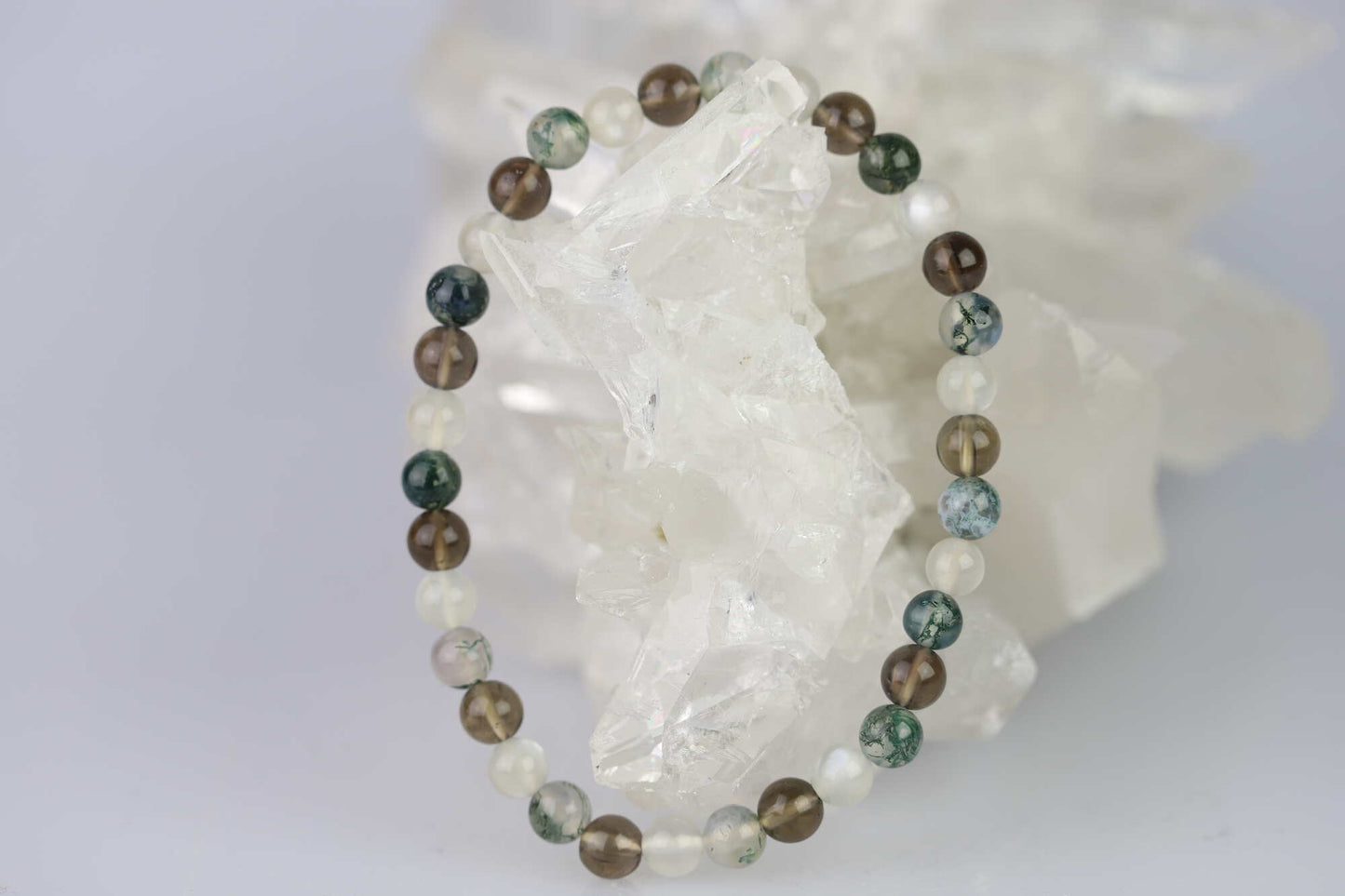 Kristallwerk präsentiert: Armband mit polierten Mondstein & Moosachat & Rauchquarz Kugeln auf einer Bergkristall Stufe.