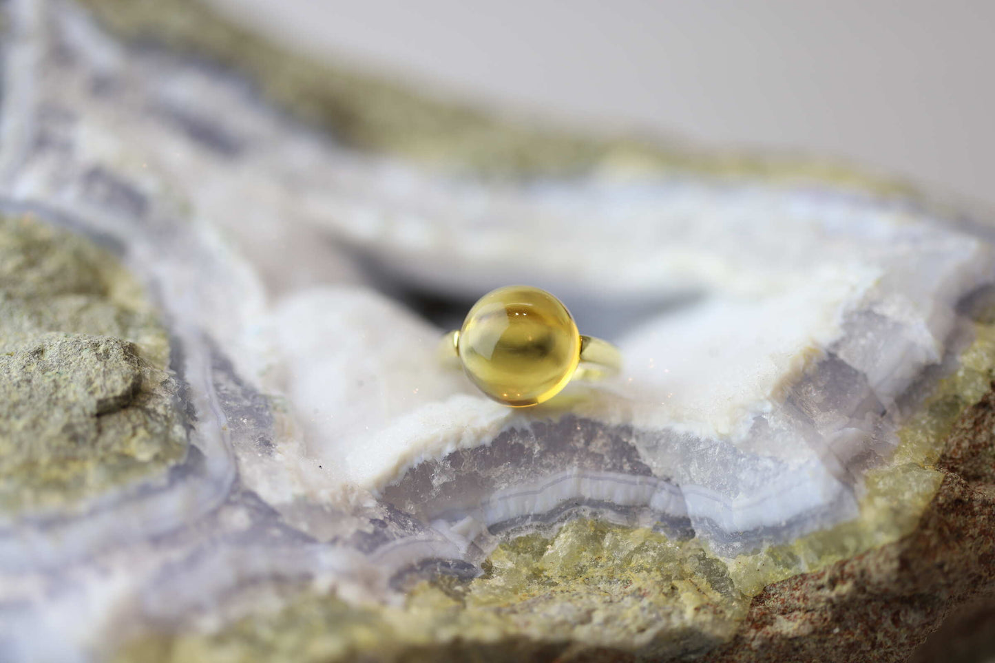 Kristallwerk präsentiert einen Ring aus Gold mit einem goldfarbigen und klaren Citrin auf einer Chalcedongeode.