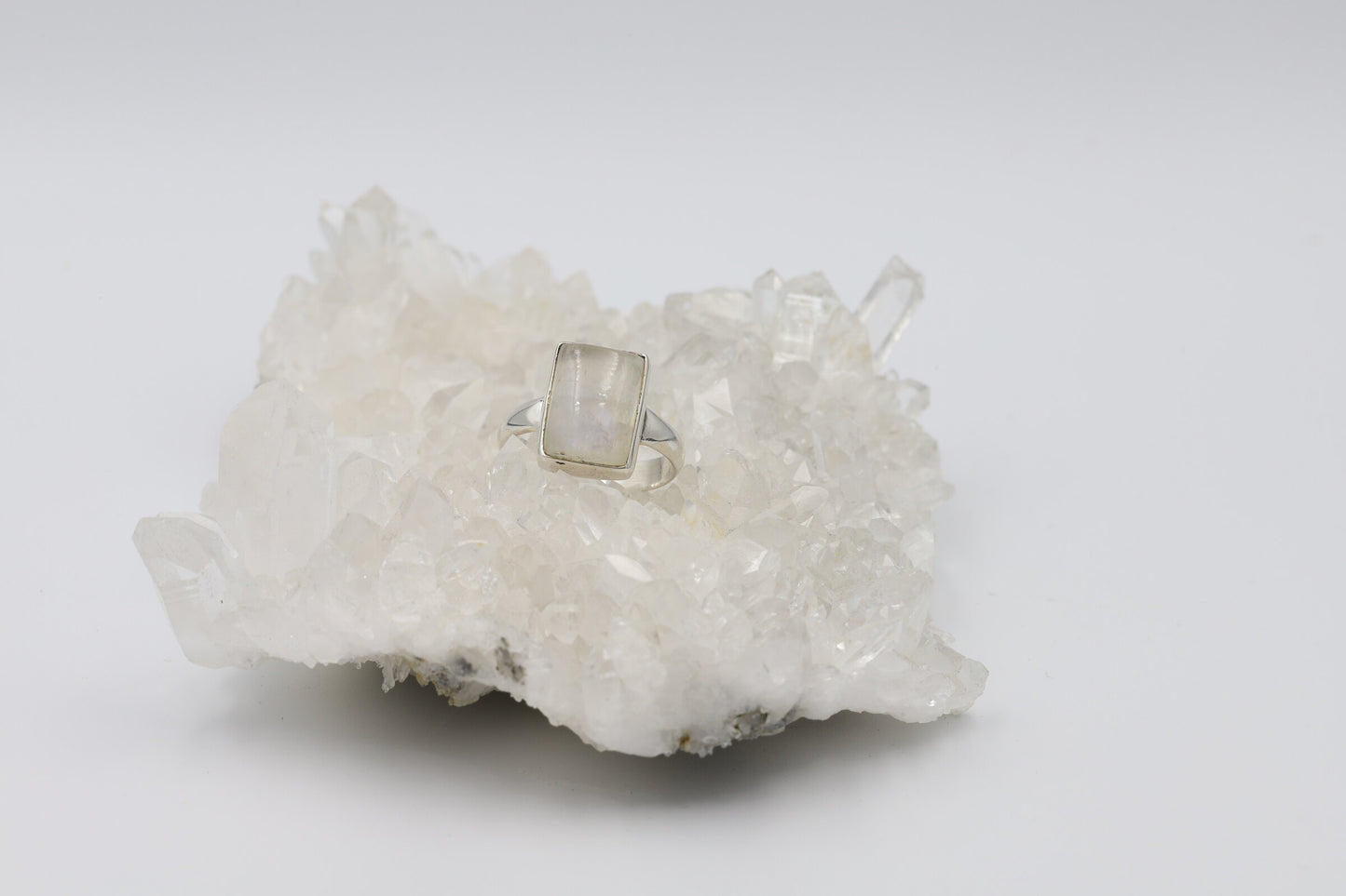 Kristallwerk präsentiert einen Ring aus Silber 925 mit einem polierten und irisierenden Mondstein Cabochon auf einer Bergkristallstufe