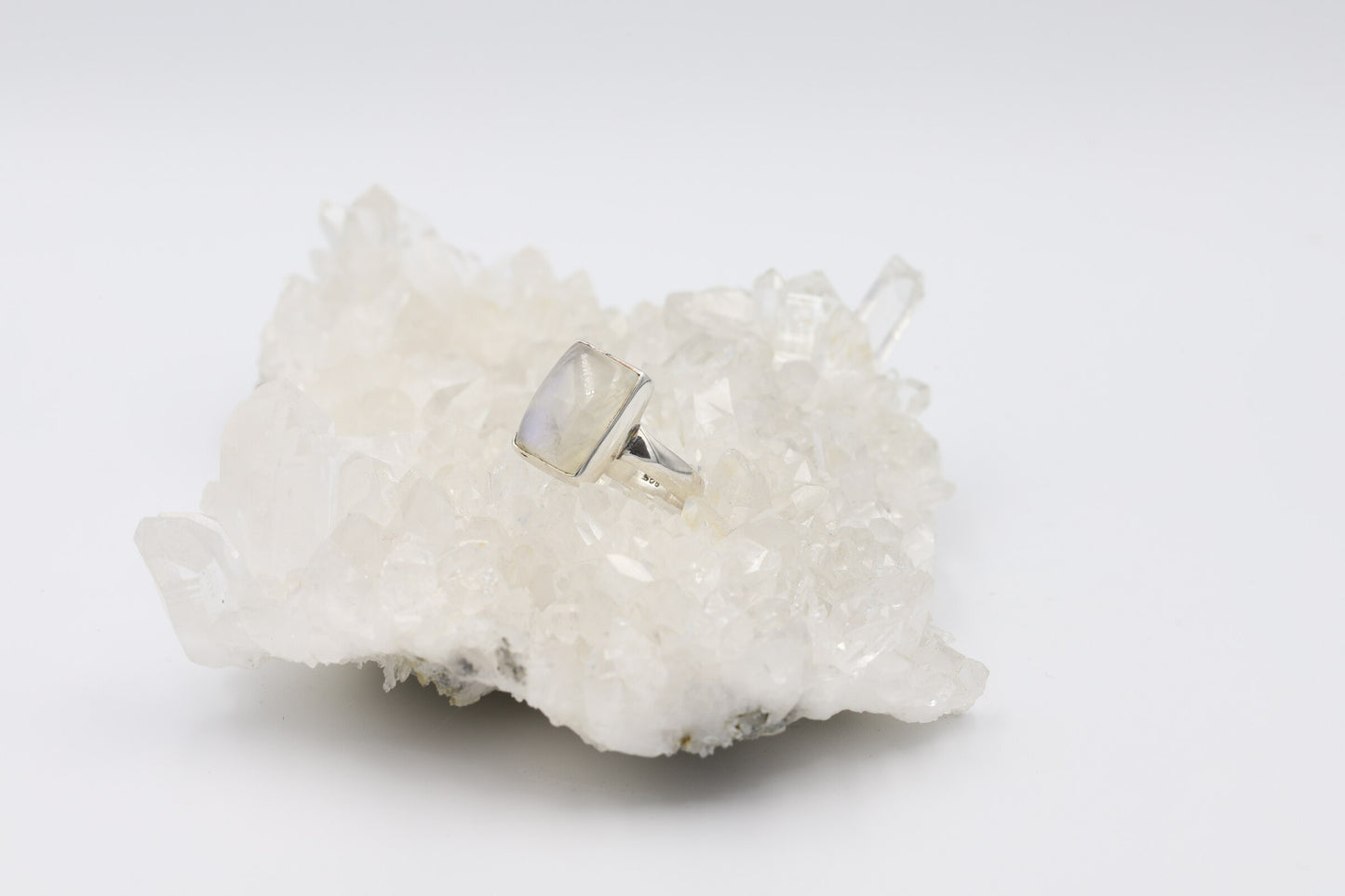 Kristallwerk präsentiert einen Ring aus Silber 925 mit einem polierten und irisierenden Mondstein Cabochon auf einer Bergkristallstufe