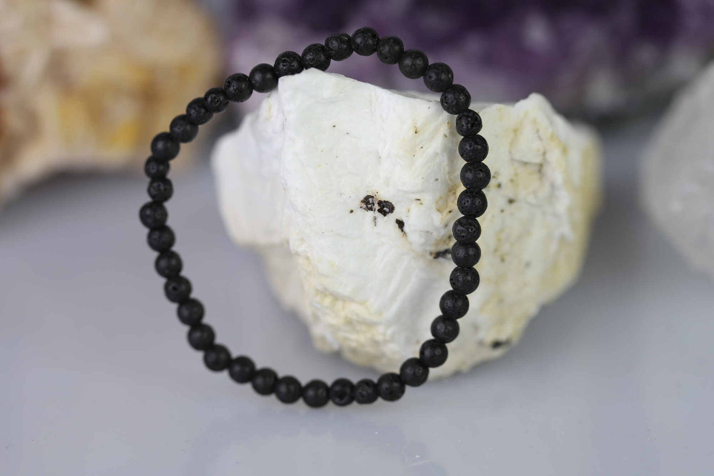 Kristallwerk präsentiert: Armband aus matten Lava-Stein Kugeln angelehnt an einem Barytstein.