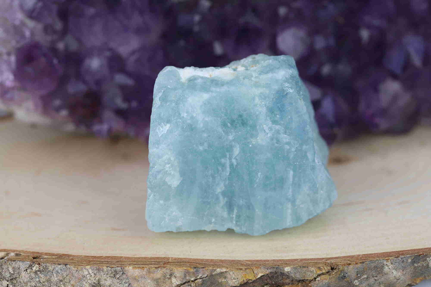 Kristallwerk präsentiert: Rohe Schätze, roher hellblauer Aquamarin vor einer Amethyststufe.