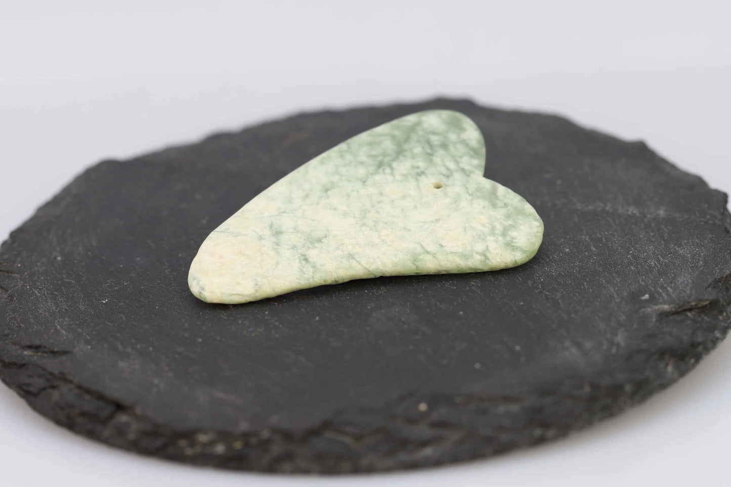 Kristallwerk präsentiert: Geschliffene Schätze Gua Sha Massagestück aus Jade auf einer Granitplatte.
