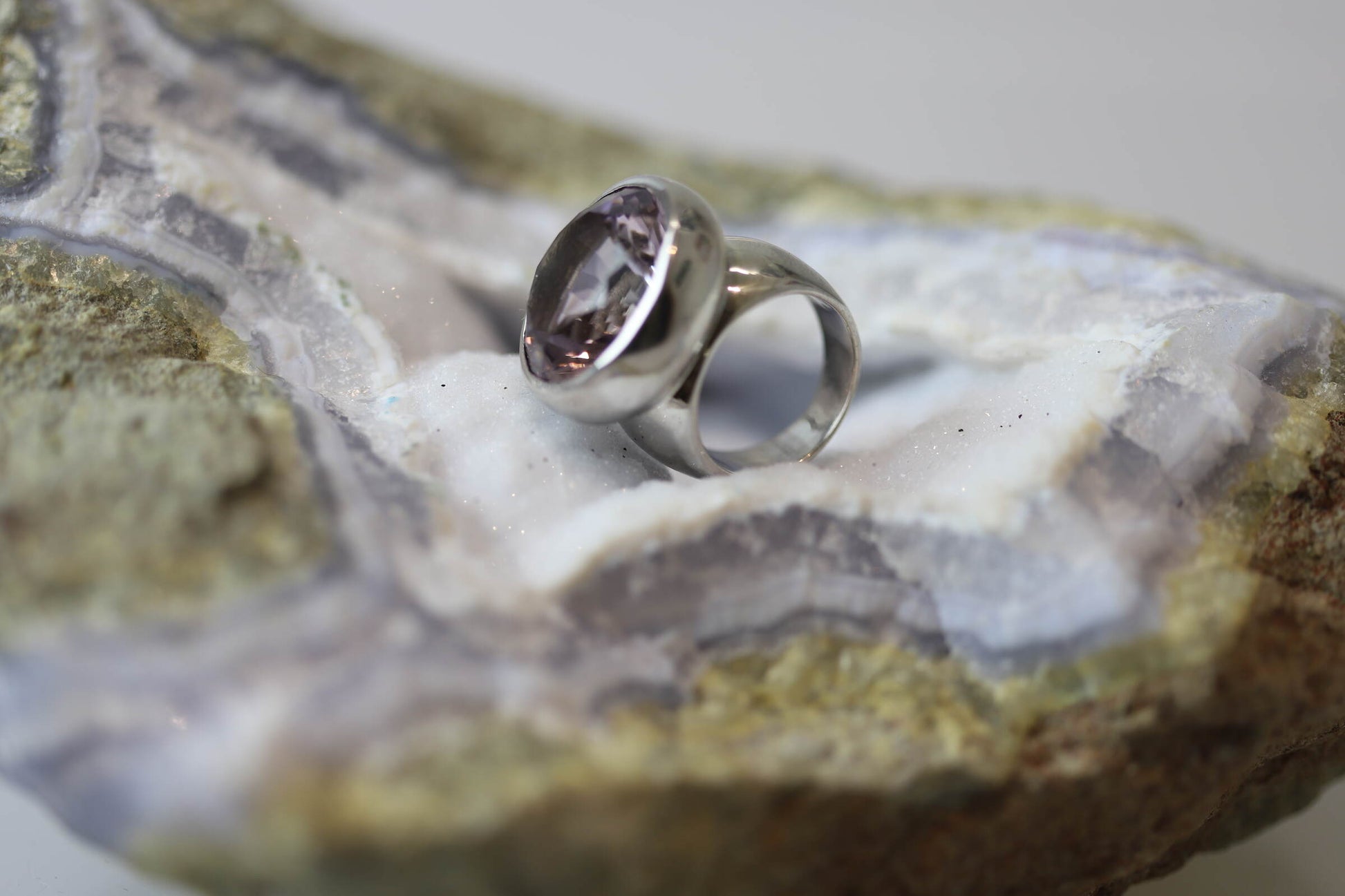 Kristallwerk präsentiert einen leuchtenden facettierten und runden Amethyst Ring aus Silber massiv auf einer Chalcedongeode..