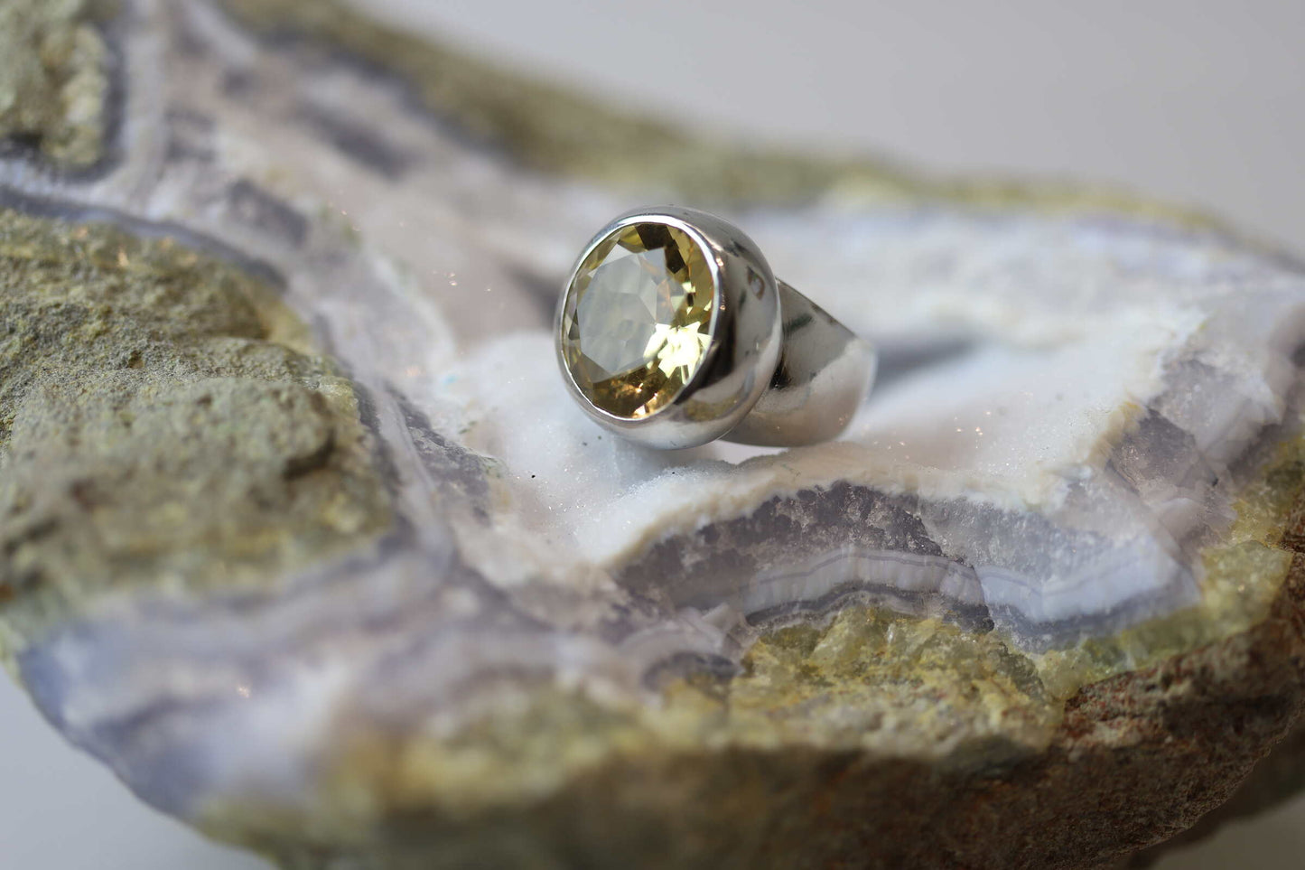 Kristallwerk präsentiert einen leuchtenden facettierten und runden Citrin Ring aus Silber massiv auf einer Chalcedongeode..