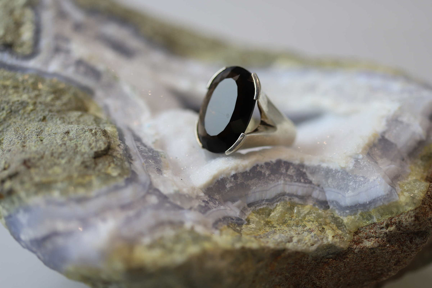 Kristallwerk präsentiert einen leuchtenden facettierten und ovalen Rauchquarz Ring aus Silber massiv auf einer Chalcedongeode..