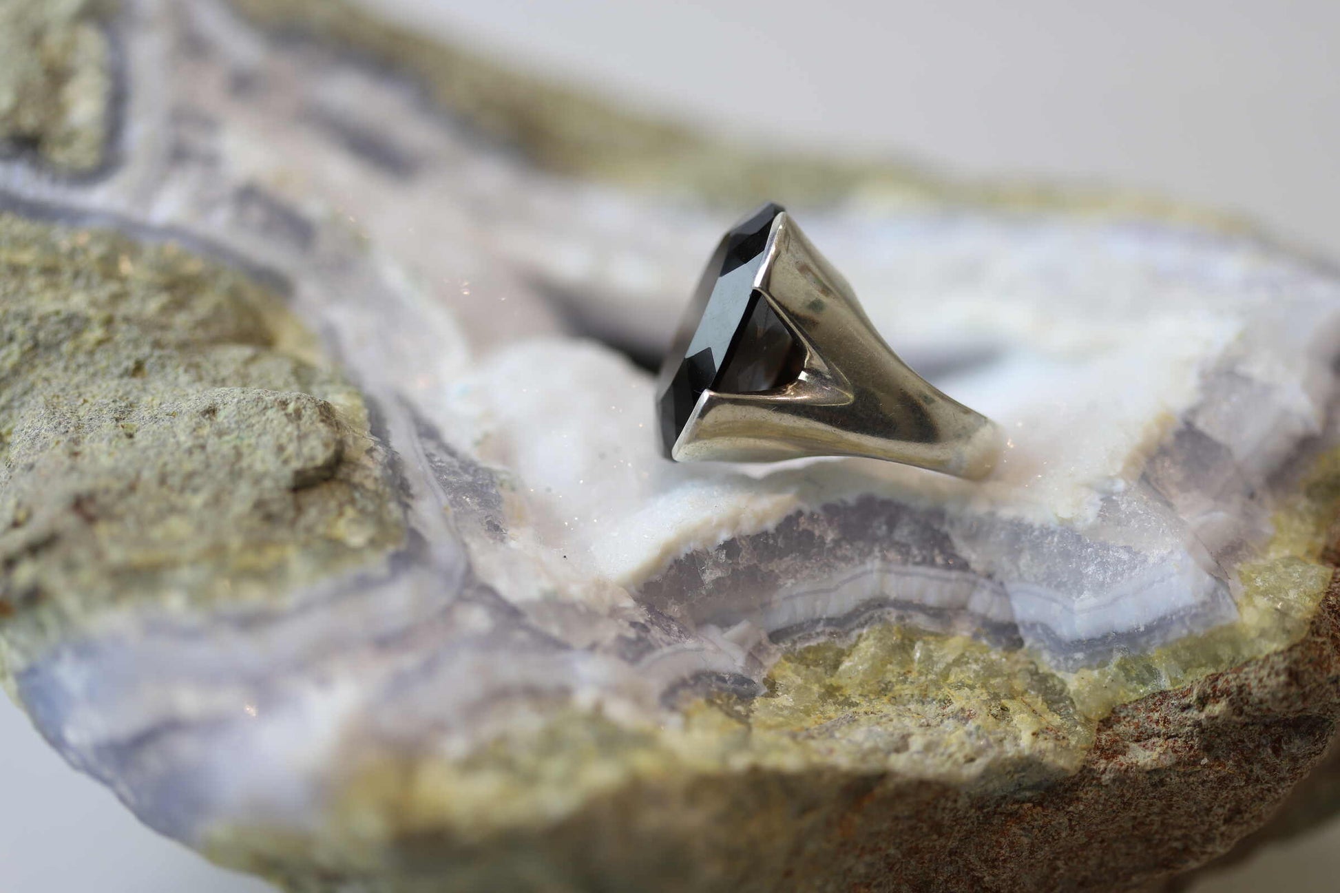 Kristallwerk präsentiert einen leuchtenden facettierten und ovalen Rauchquarz Ring aus Silber massiv auf einer Chalcedongeode..