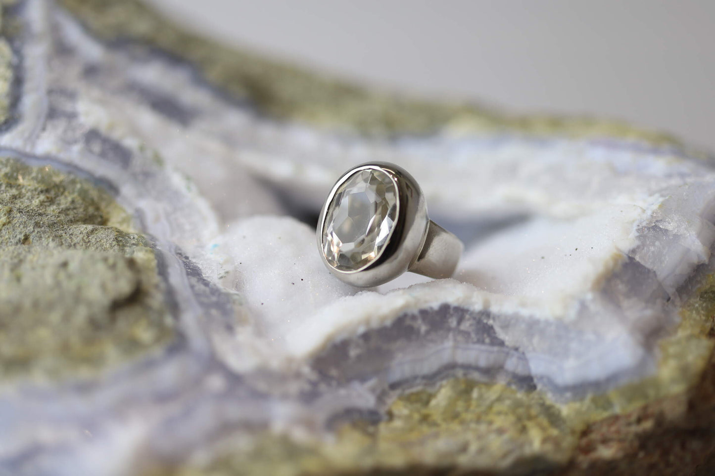 Kristallwerk präsentiert einen Ring aus Silber 925 mit facettiertem und glasklarem Bergkristall auf einer Chalcedongeode.