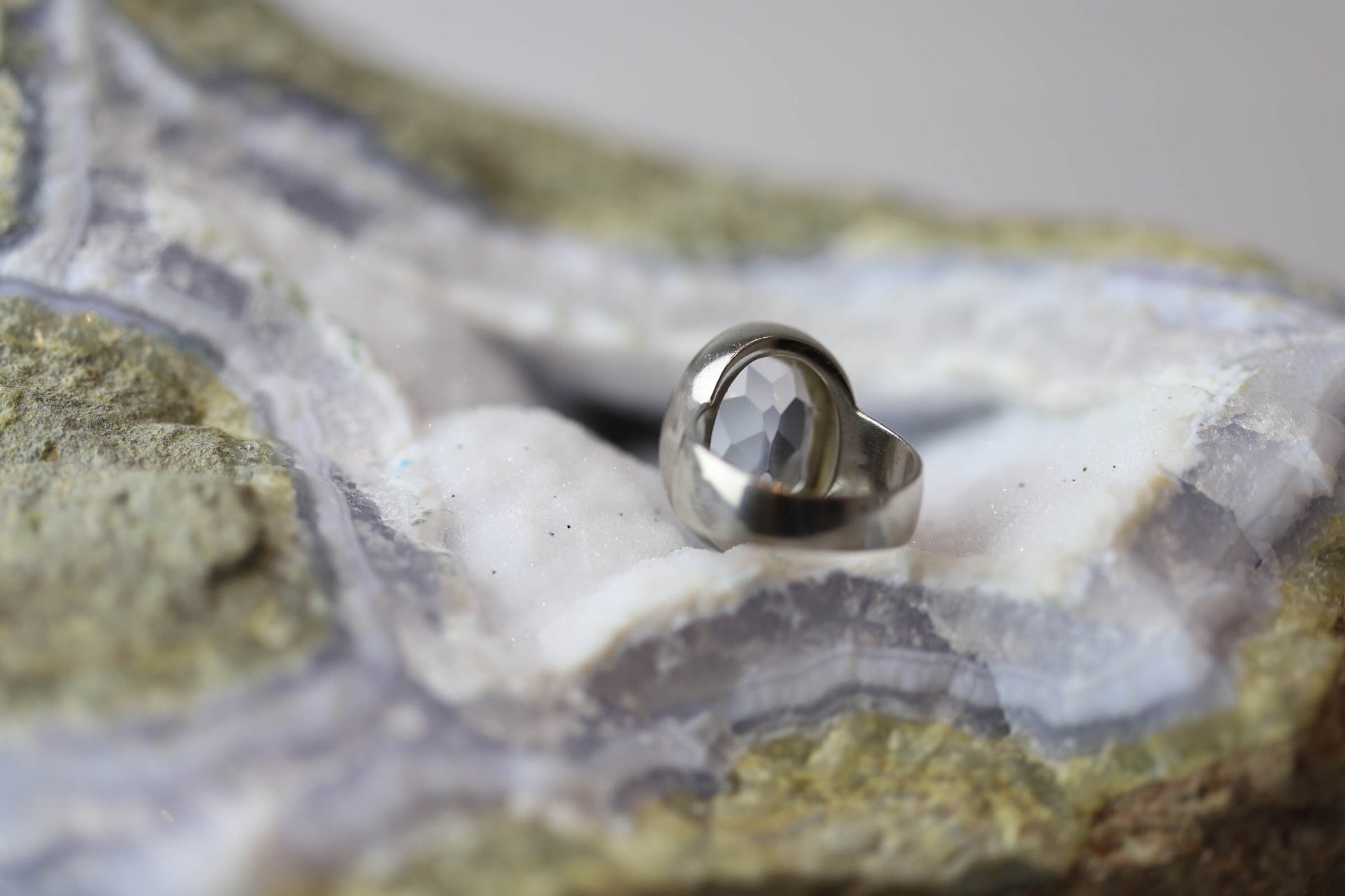 Kristallwerk präsentiert einen Ring aus Silber 925 mit facettiertem und glasklarem Bergkristall auf einer Chalcedongeode.