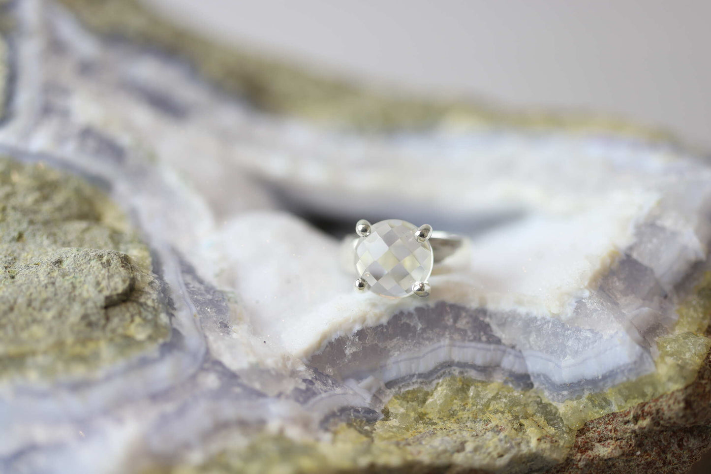 Kristallwerk präsentiert einen Ring aus Silber 925 mit facettiertem und glasklarem Bergkristall auf einer Chalcedongeode.