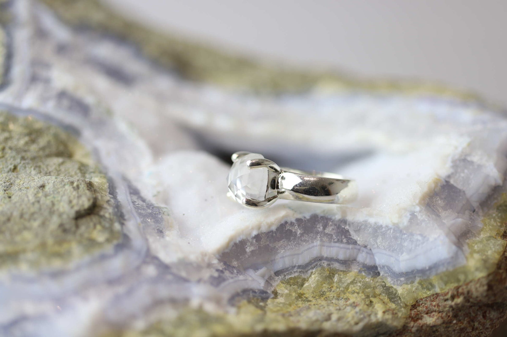 Kristallwerk präsentiert einen Ring aus Silber 925 mit facettiertem und glasklarem Bergkristall auf einer Chalcedongeode.