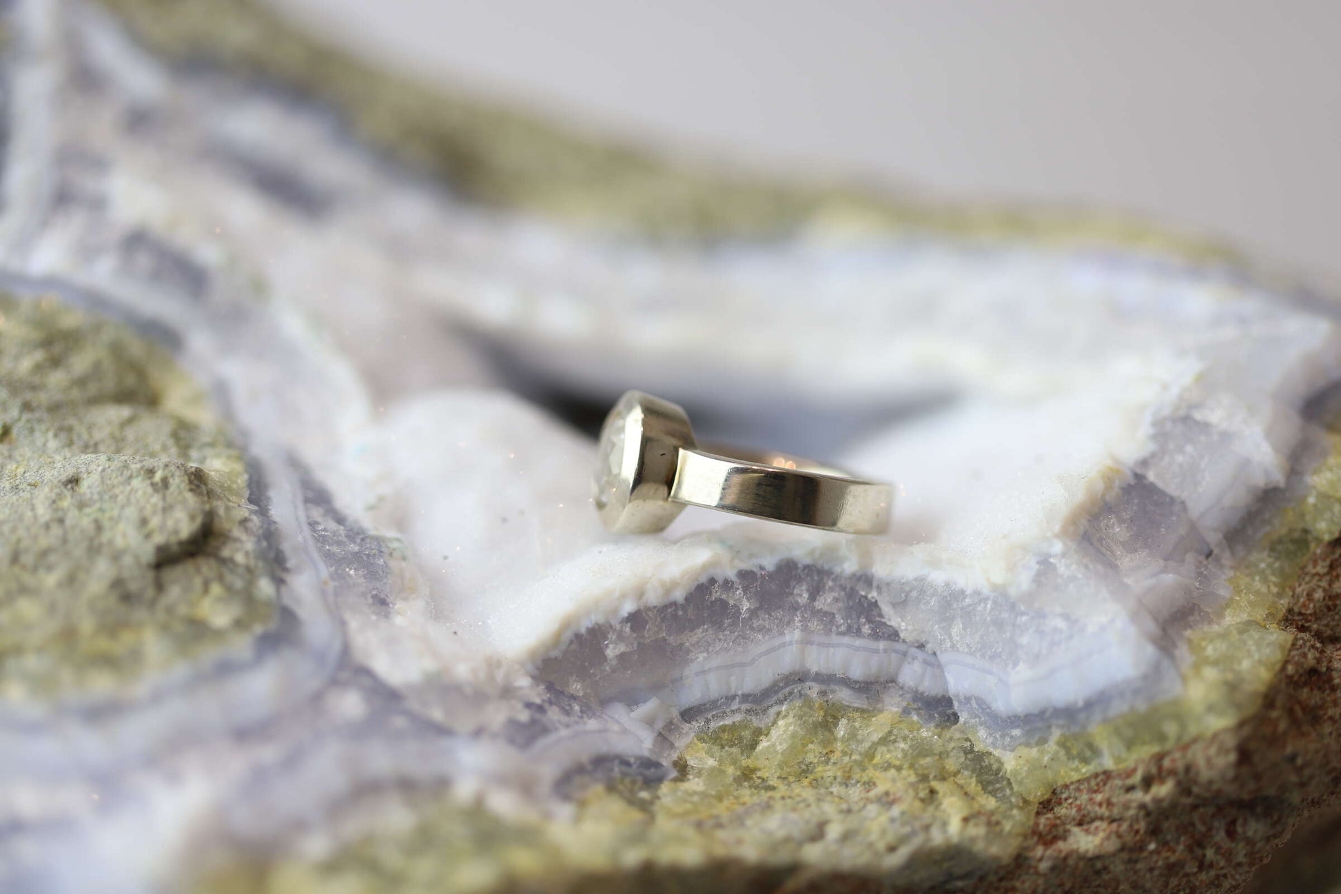 Kristallwerk präsentiert einen Ring aus Silber 925 mit facettiertem und glasklarem Bergkristall auf einer Chalcedongeode.