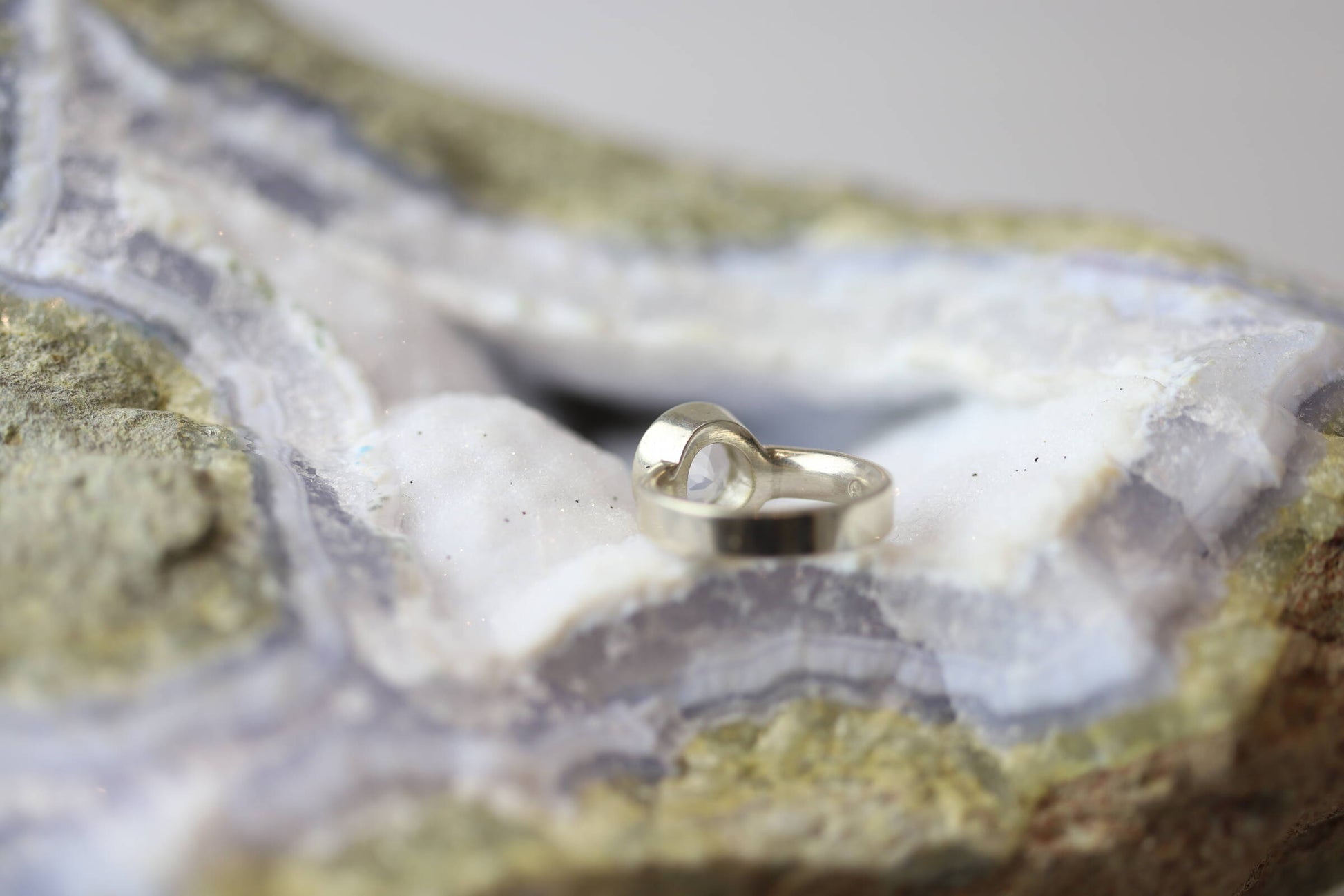 Kristallwerk präsentiert einen Ring aus Silber 925 mit facettiertem und glasklarem Bergkristall auf einer Chalcedongeode.