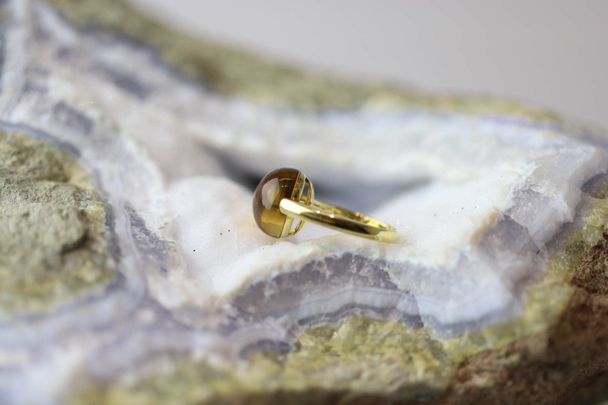 Kristallwerk präsentiert einen Ring aus Gold mit einem goldfarbigen und klaren Citrin auf einer Chalcedongeode.