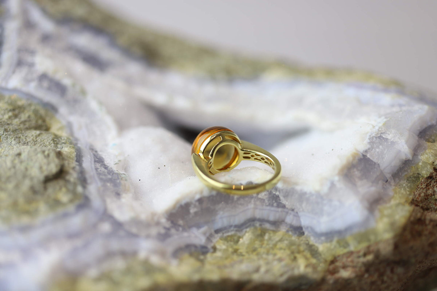 Kristallwerk präsentiert einen Ring aus Gold mit einem goldfarbigen und klaren Citrin auf einer Chalcedongeode.