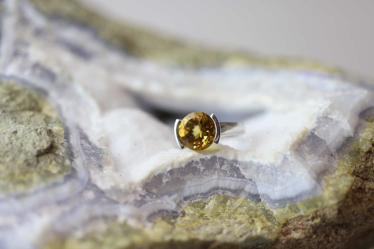 Kristallwerk präsentiert einen Ring aus Silber mit einem goldfarbigem, facettiertem und ovalem Citrin auf einer Chalcedongeode.