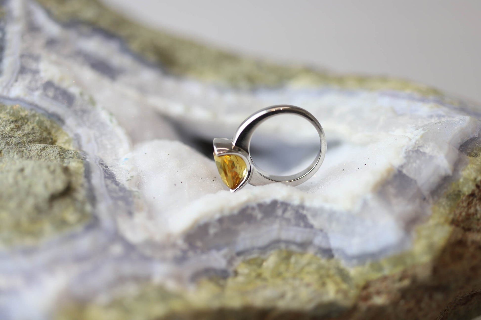 Kristallwerk präsentiert einen Ring aus Silber mit einem goldfarbigem, facettiertem und ovalem Citrin auf einer Chalcedongeode.