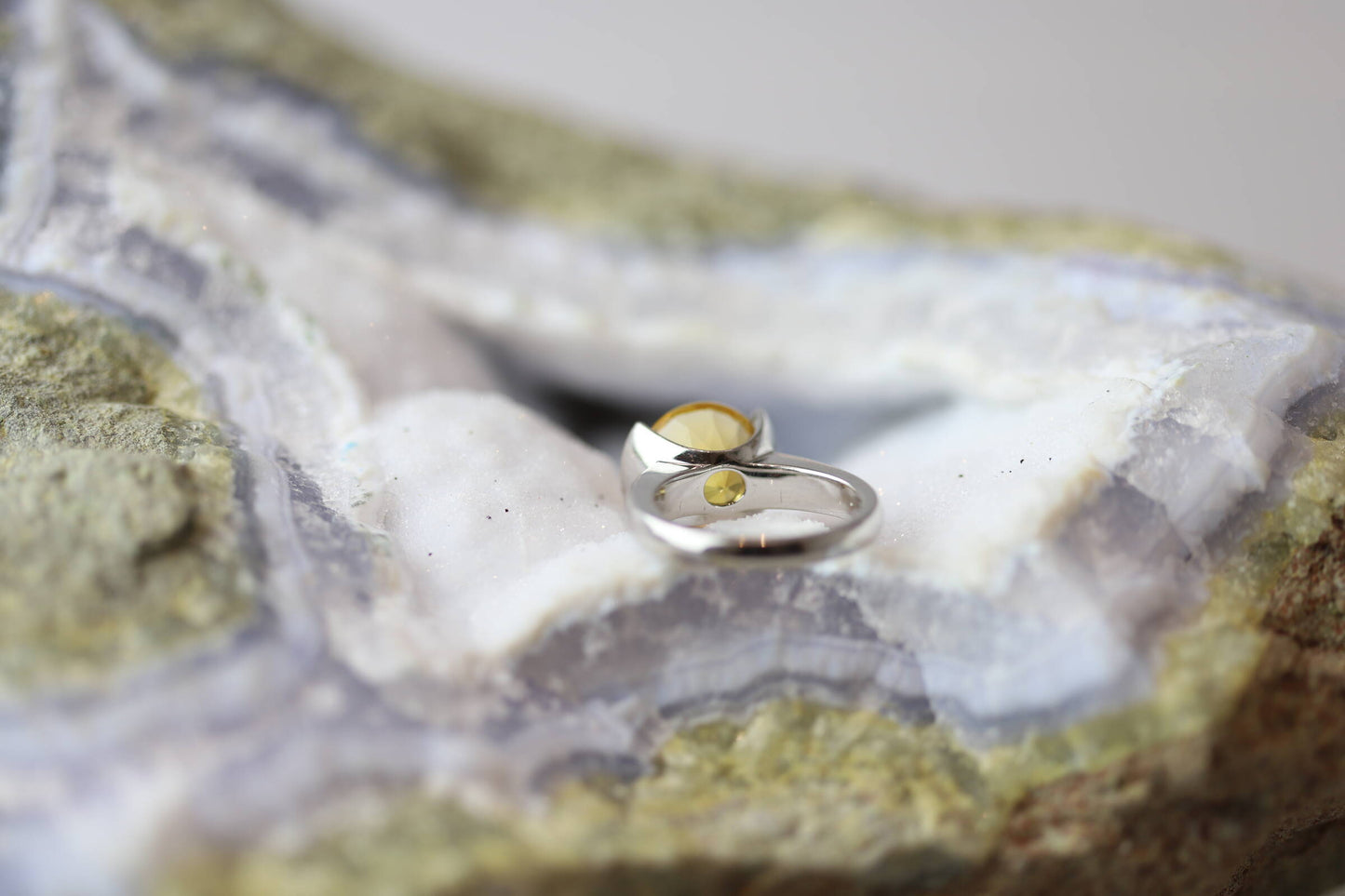 Kristallwerk präsentiert einen Ring aus Silber mit einem goldfarbigem, facettiertem und ovalem Citrin auf einer Chalcedongeode.