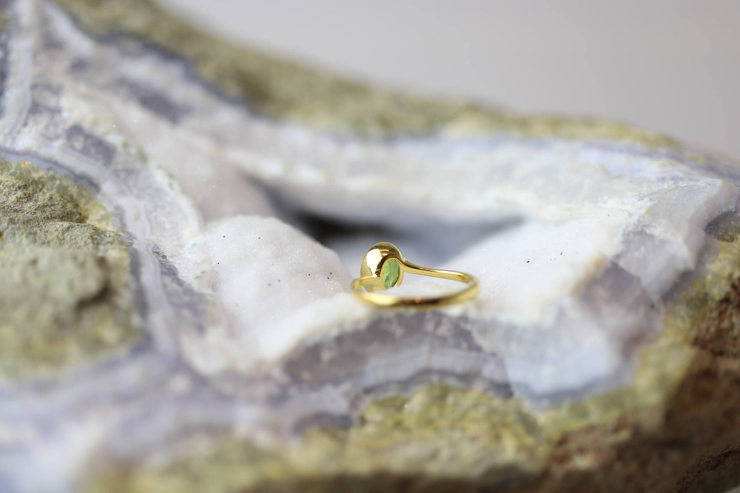 Kristallwerk präsentiert einen Ring aus Silber vergoldet mit einem facettiertem und ovalem Peridot auf einer Chalcedongeode.