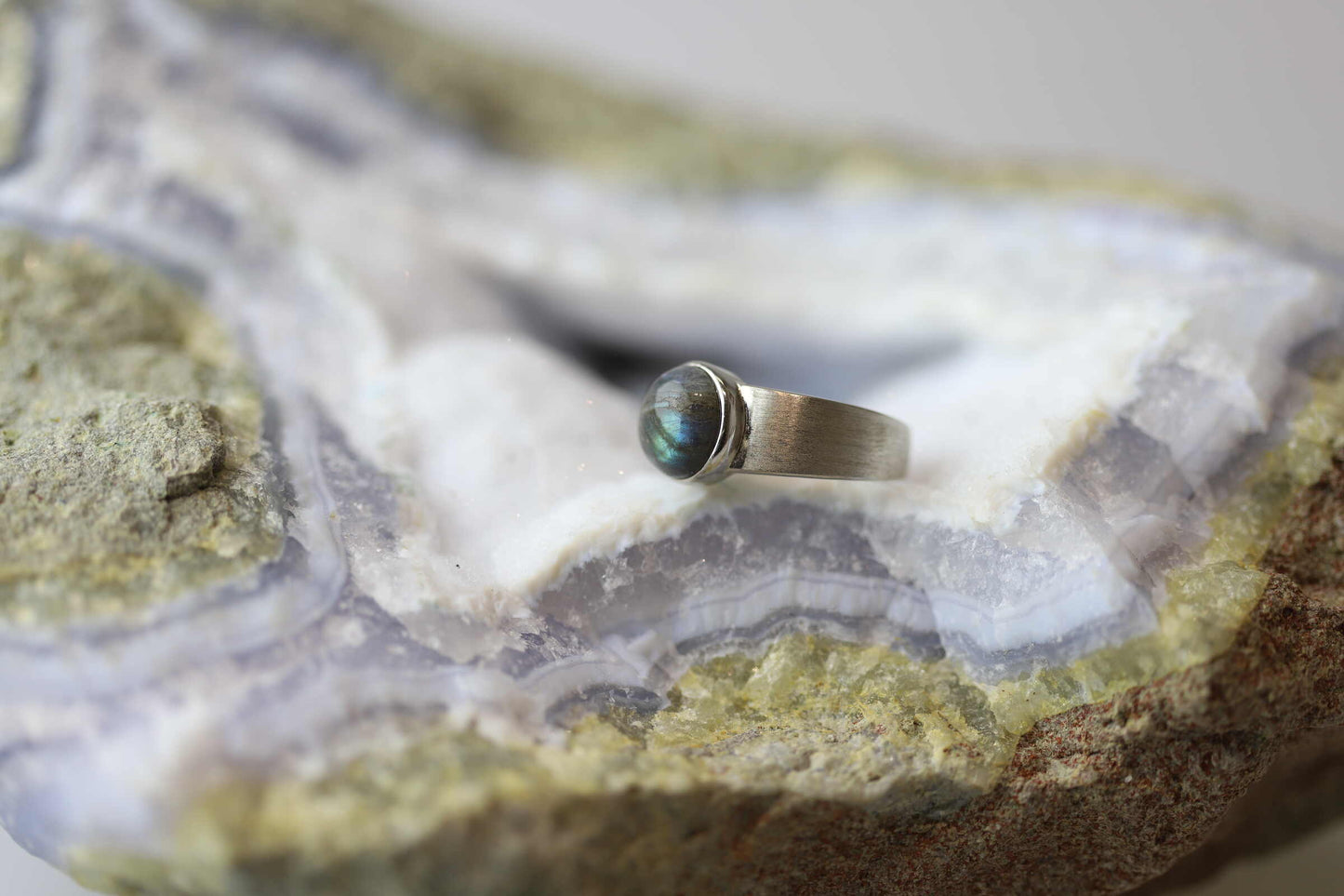 Kristallwerk präsentiert einen Ring aus Silber 925 mit einem polierten und irisierenden Labradorit Cabochon auf einer Chalcedongeode.