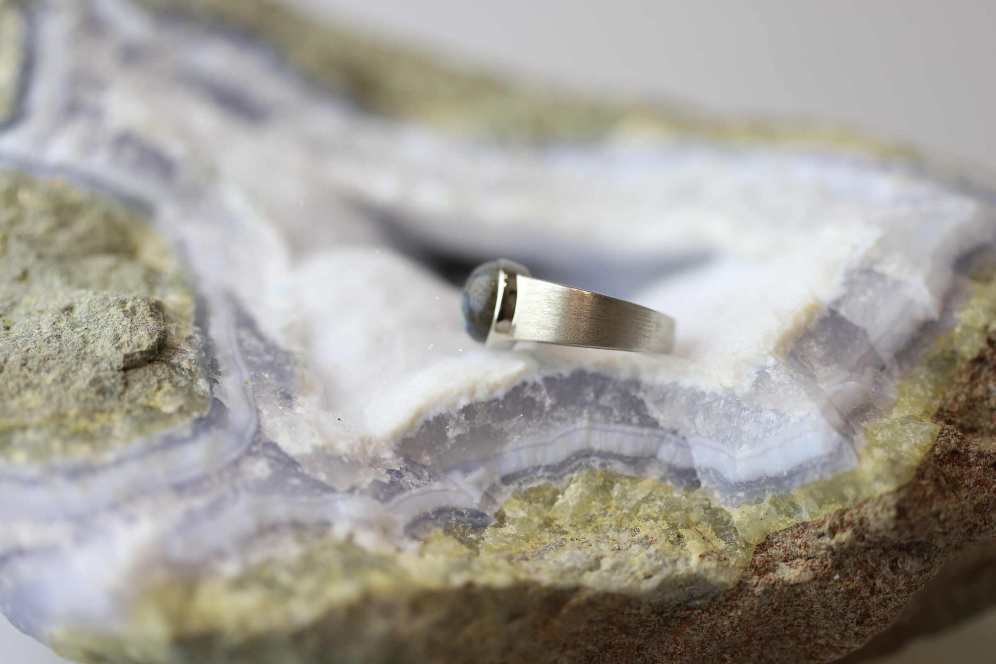 Kristallwerk präsentiert einen Ring aus Silber 925 mit einem polierten und irisierenden Labradorit Cabochon auf einer Chalcedongeode.