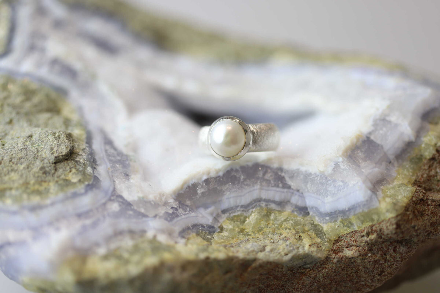 Kristallwerk präsentiert einen Ring aus Silber 925 mit einer polierten und glänzenden Süsswasserperle auf einer Chalcedongeode.