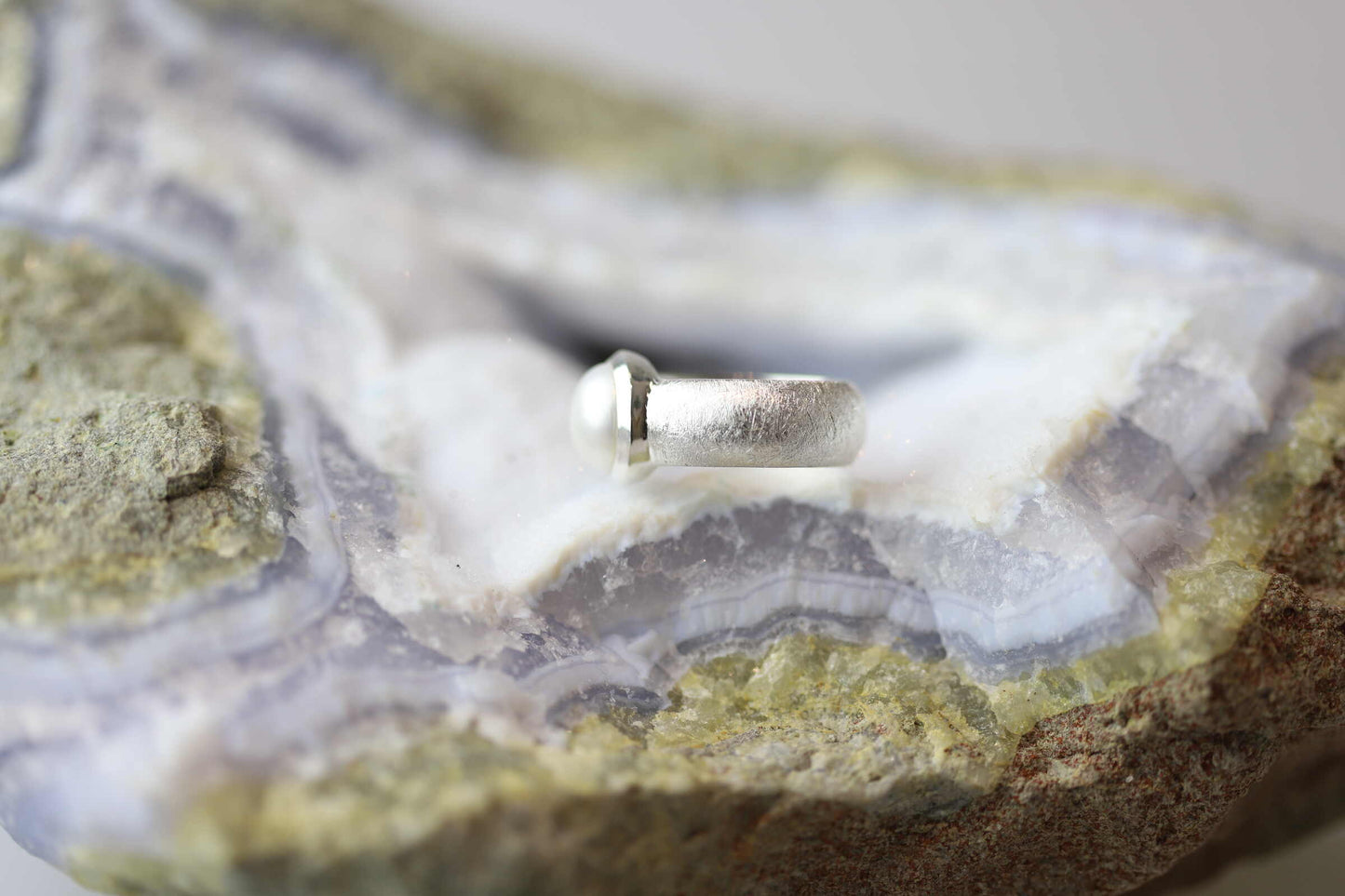 Kristallwerk präsentiert einen Ring aus Silber 925 mit einer polierten und glänzenden Süsswasserperle auf einer Chalcedongeode.