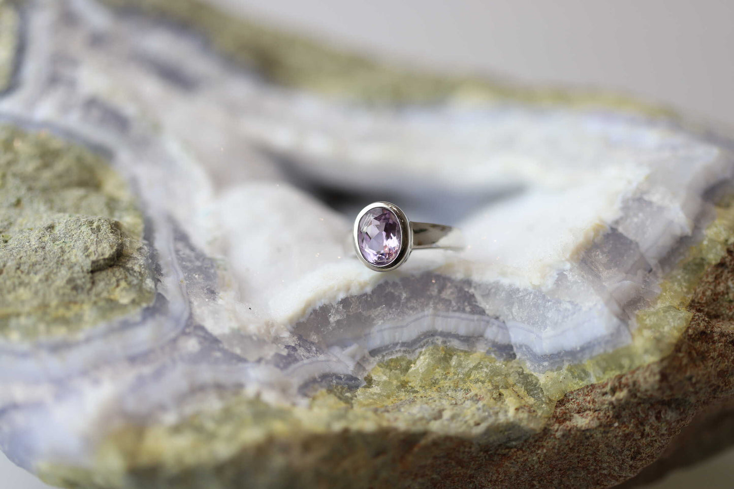 Kristallwerk präsentiert einen Ring aus Silber 925 mit einem facettierten und leuchtenden Amethyst auf einer Chalcedongeode