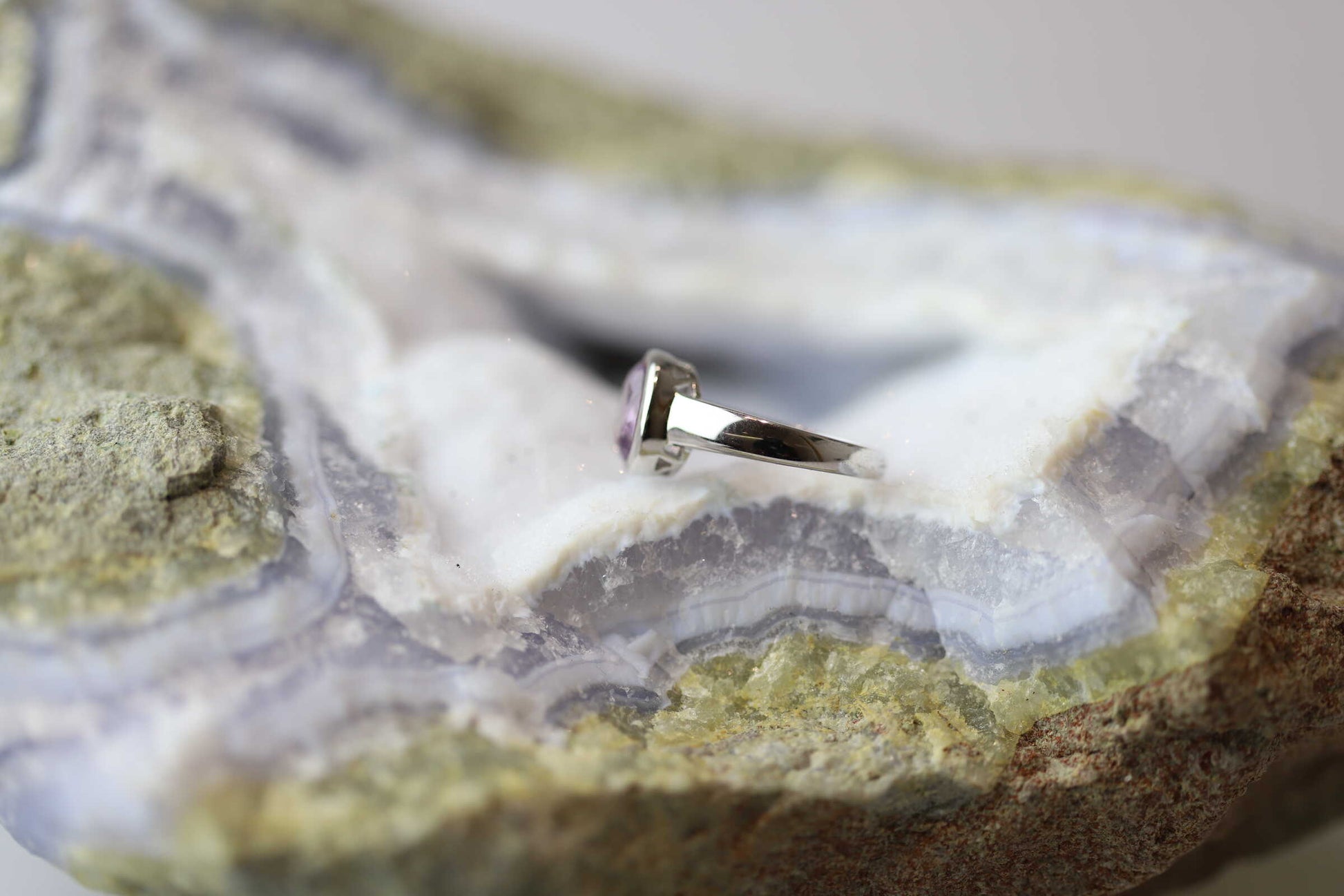 Kristallwerk präsentiert einen Ring aus Silber 925 mit einem facettierten und leuchtenden Amethyst auf einer Chalcedongeode