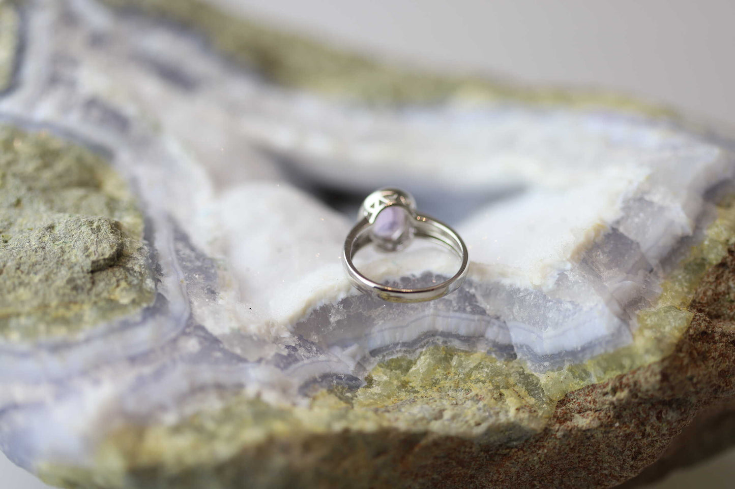 Kristallwerk präsentiert einen Ring aus Silber 925 mit einem facettierten und leuchtenden Amethyst auf einer Chalcedongeode