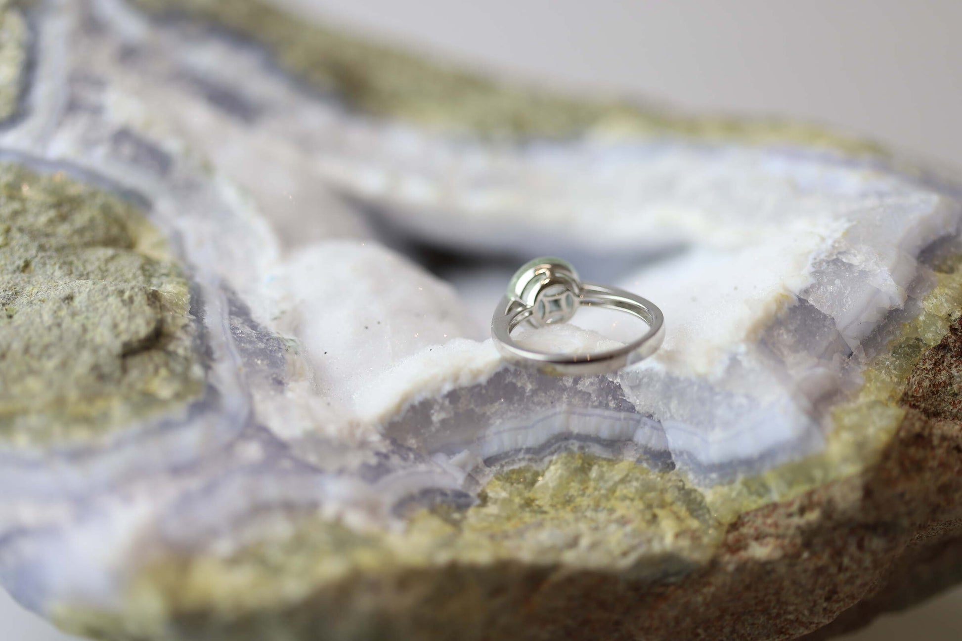 Kristallwerk präsentiert einen Ring aus Silber 925 mit einem facettierten und leuchtenden Präsiolith auf einer Chalcedongeode