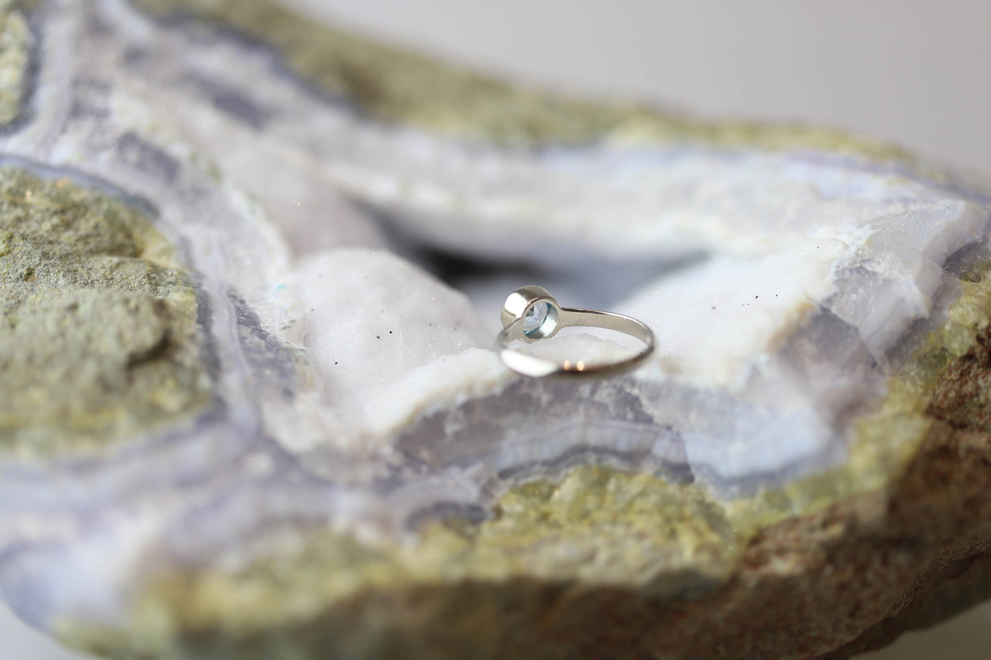 Kristallwerk präsentiert einen Ring aus Silber 925 mit einem facettierten und leuchtenden blauen Edeltopas auf einer Chalcedongeode