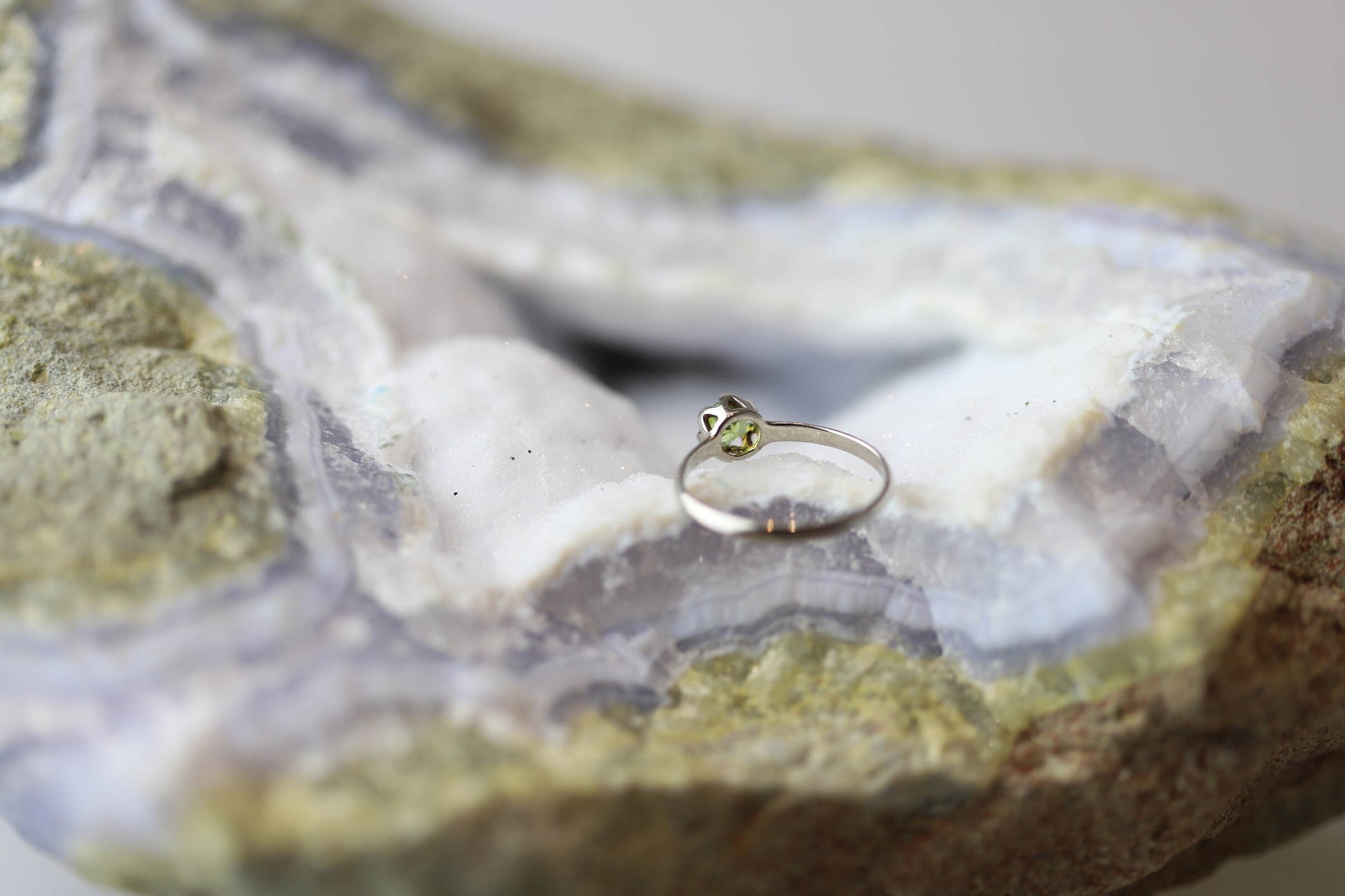 Kristallwerk präsentiert einen Ring aus Silber 925 mit einem facettierten und funkelnden Peridot auf einer Chalcedongeode.