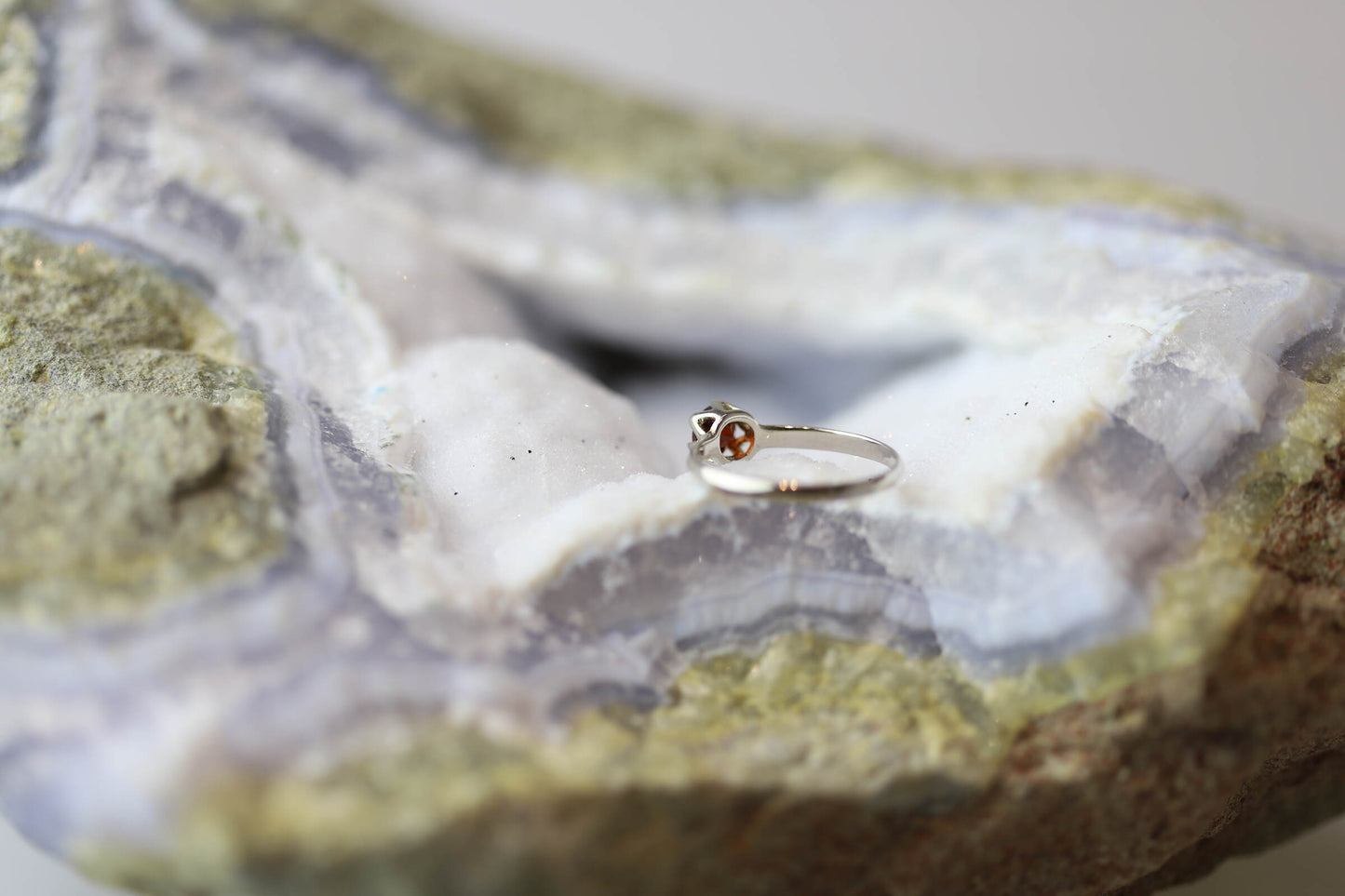 Kristallwerk präsentiert einen Ring aus Silber 925 mit einem facettierten und funkelnden Granat auf einer Chalcedongeode.