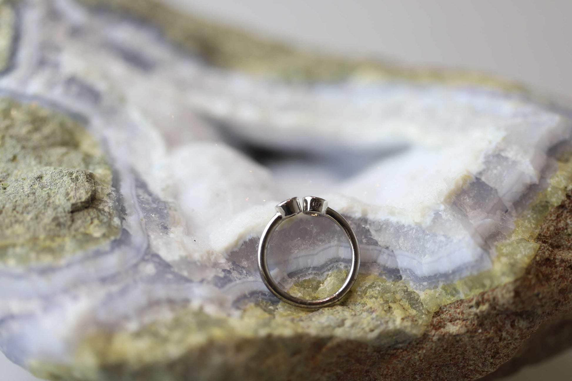 Kristallwerk präsentiert einen Ring aus Silber 925 mit zwei facettierten weissen Edeltopas auf einer Chalcedongeode.