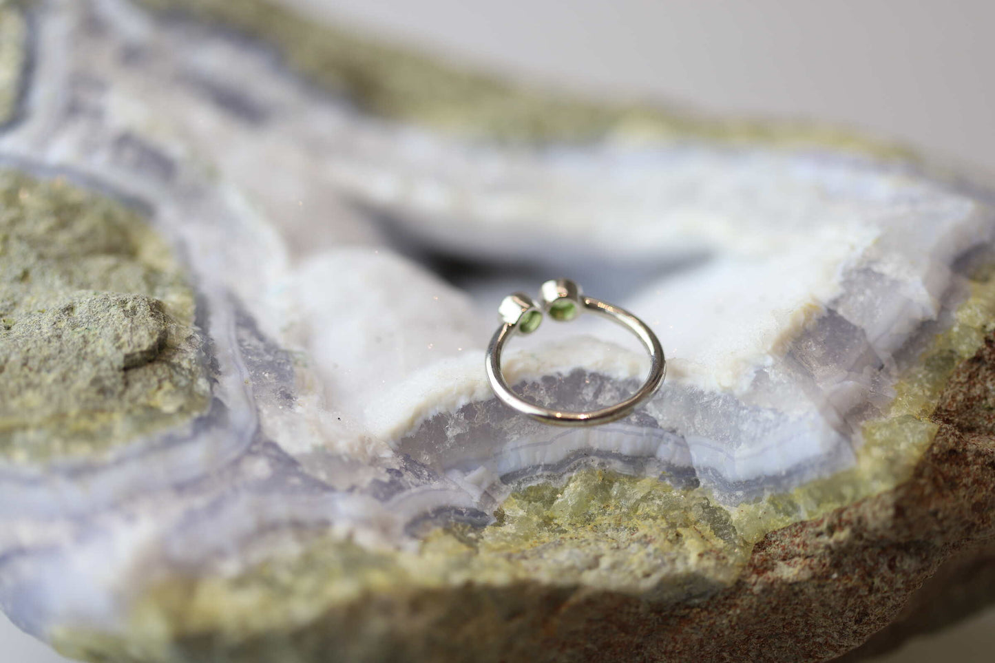 Kristallwerk präsentiert einen Ring aus Silber 925 mit zwei facettierten grünen Peridots auf einer Chalcedongeode.