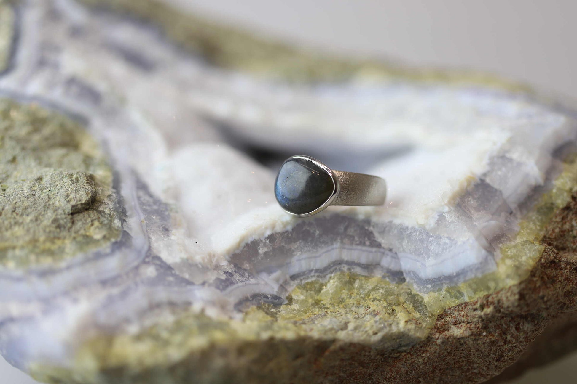 Kristallwerk präsentiert einen Ring aus Silber 925 mit einem polierten und irisierenden Labradorit auf einer Chalcedongeode.