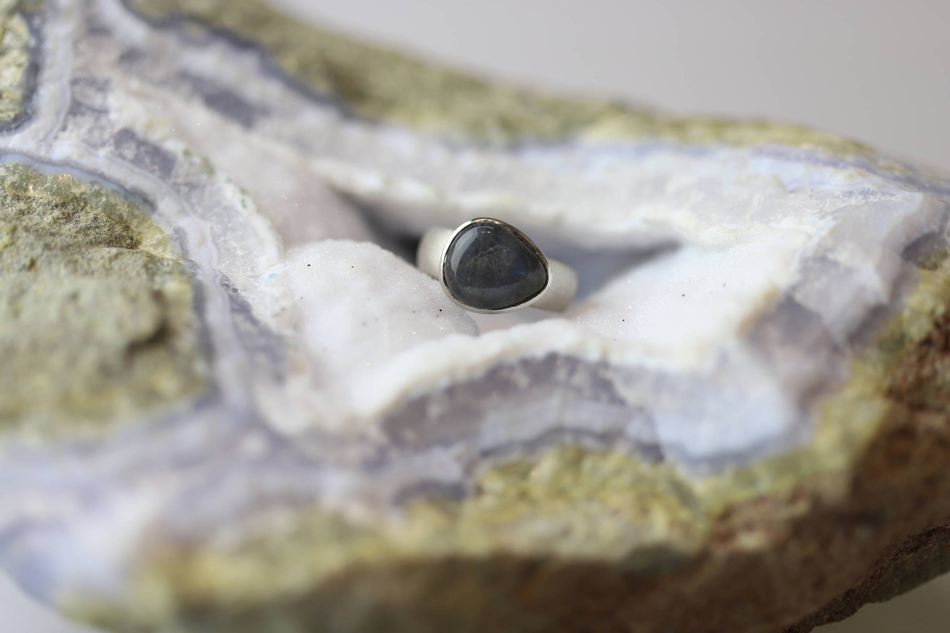 Kristallwerk präsentiert einen Ring aus Silber 925 mit einem polierten und irisierenden Labradorit auf einer Chalcedongeode.