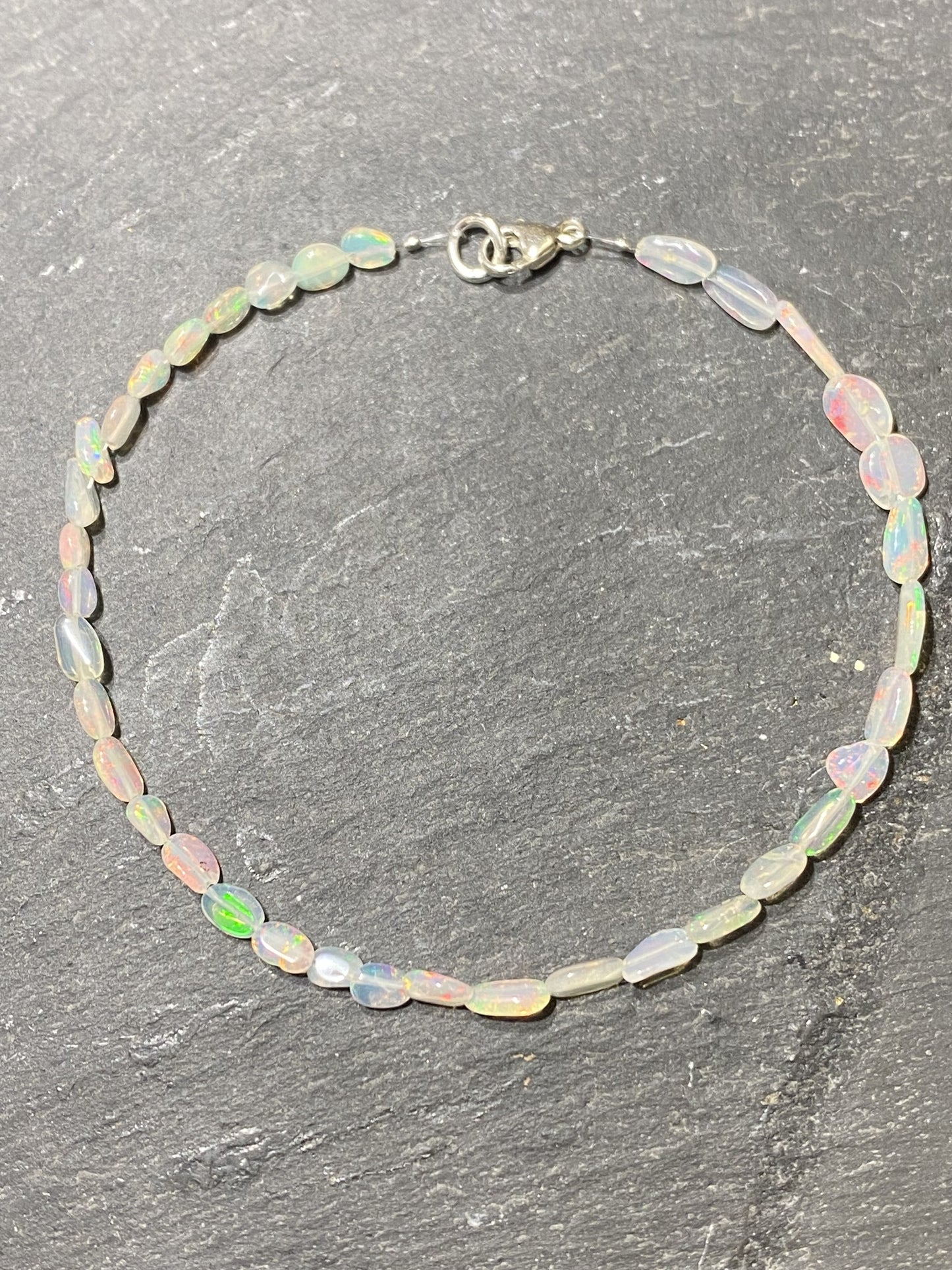 Kristallwerk präsentiert ein irisierendes Opal Armband mit Silberverschluss auf einer Granit Platte.