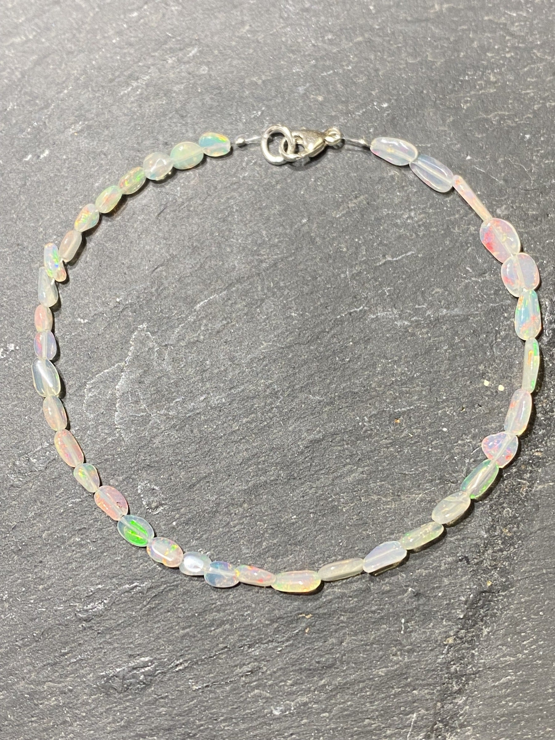 Kristallwerk präsentiert ein irisierendes Opal Armband mit Silberverschluss auf einer Granit Platte.