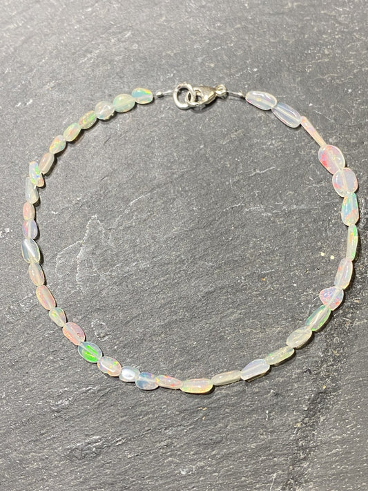 Kristallwerk präsentiert ein irisierendes Opal Armband mit Silberverschluss auf einer Granit Platte.