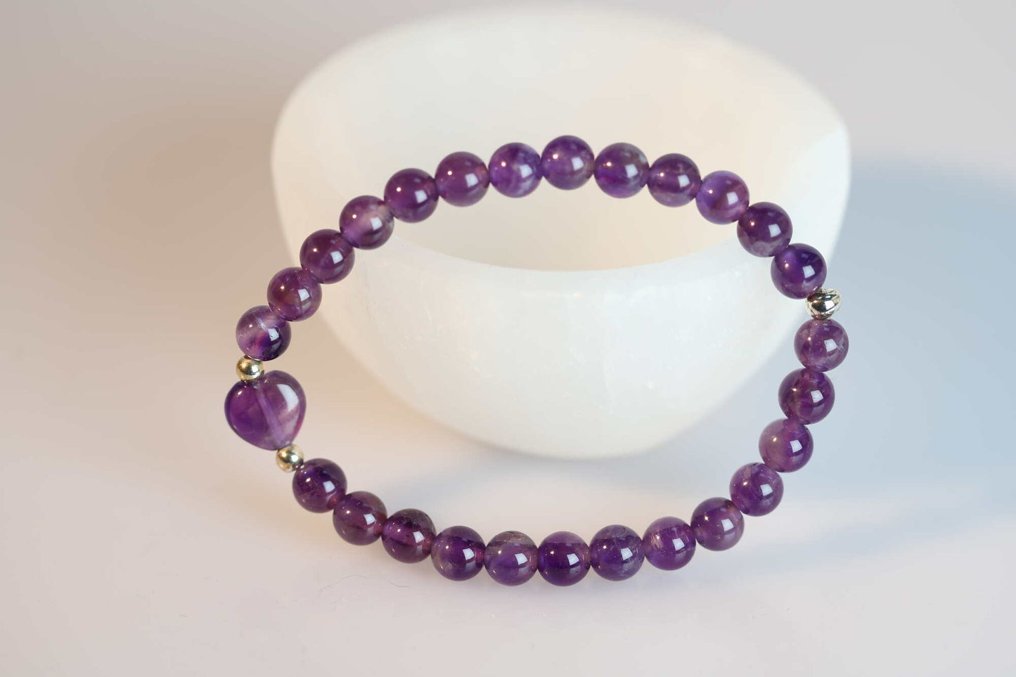 Kristallwerk präsentiert: Armband Amethyst mit Herz und Silber angelehnt an einer weissen Steintasse.