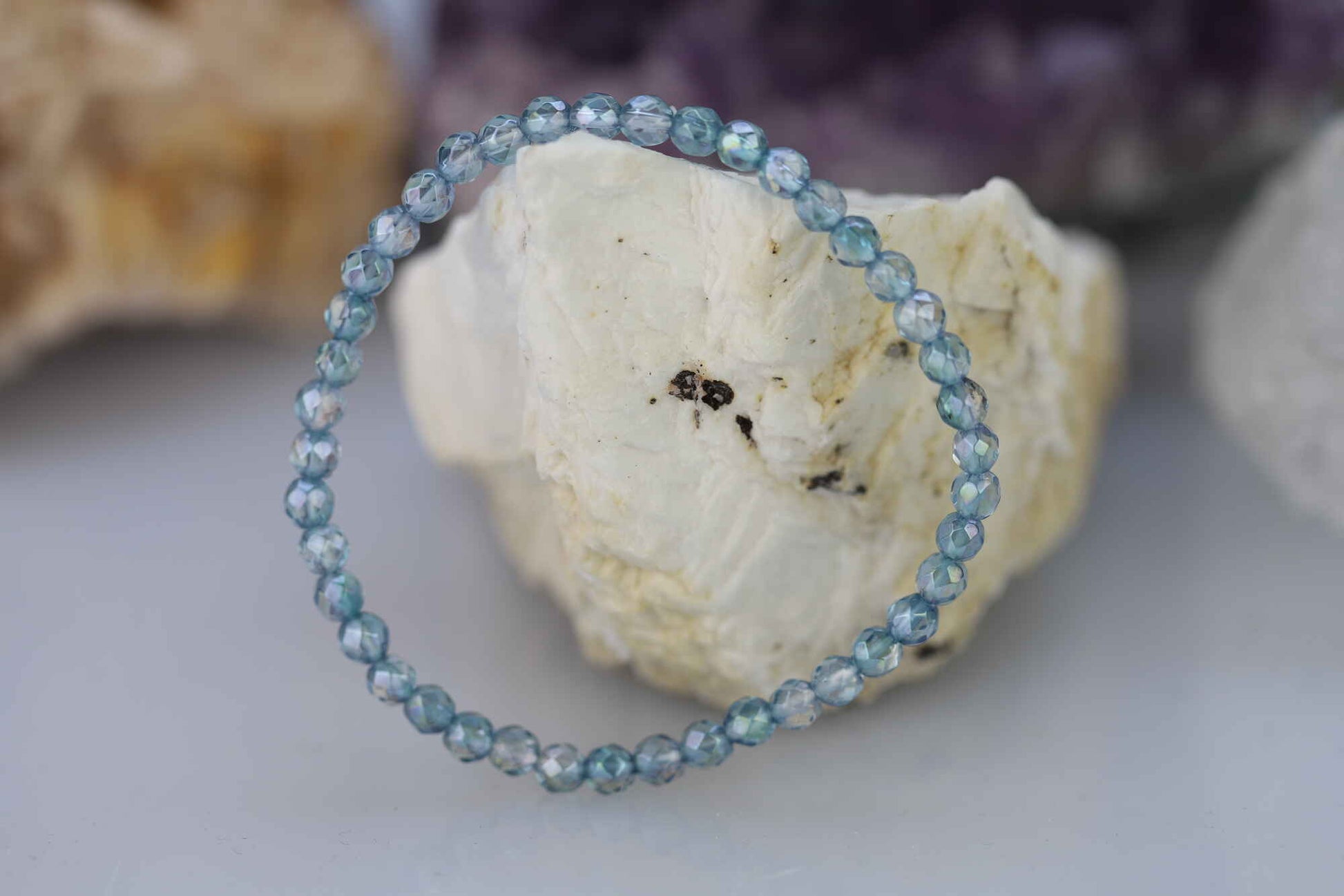 Kristallwerk präsentiert: Armband aus glänzenden und facettierten Aqua Aura Kugeln auf einem weissen Barytstein.