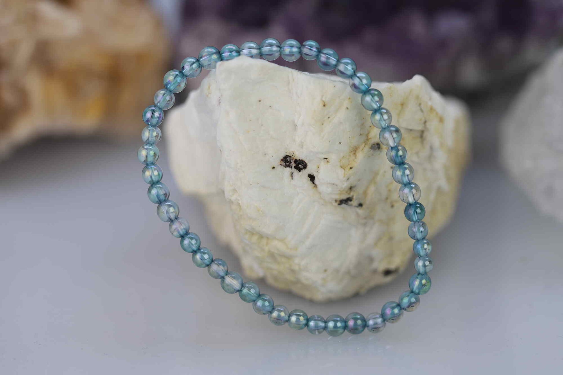 Kristallwerk präsentiert: Armband aus glänzenden Aqua Aura Kugeln auf einem weissen Barytstein.