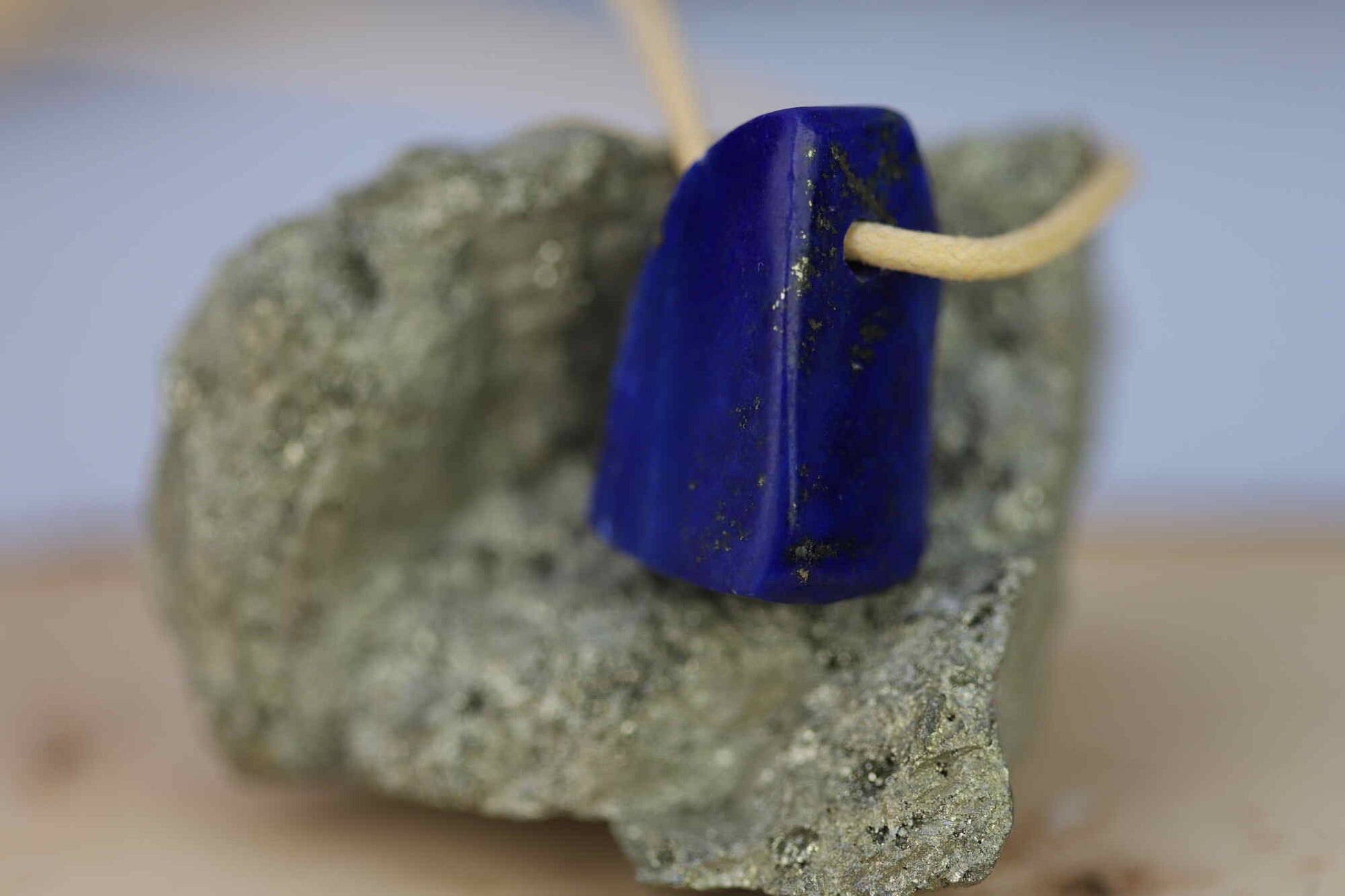 Kristallwerk präsentiert: Anhänger Lapis Lazuli auf goldenen Baumwollband aufgezogen und auf einem Pyritstein plaziert.