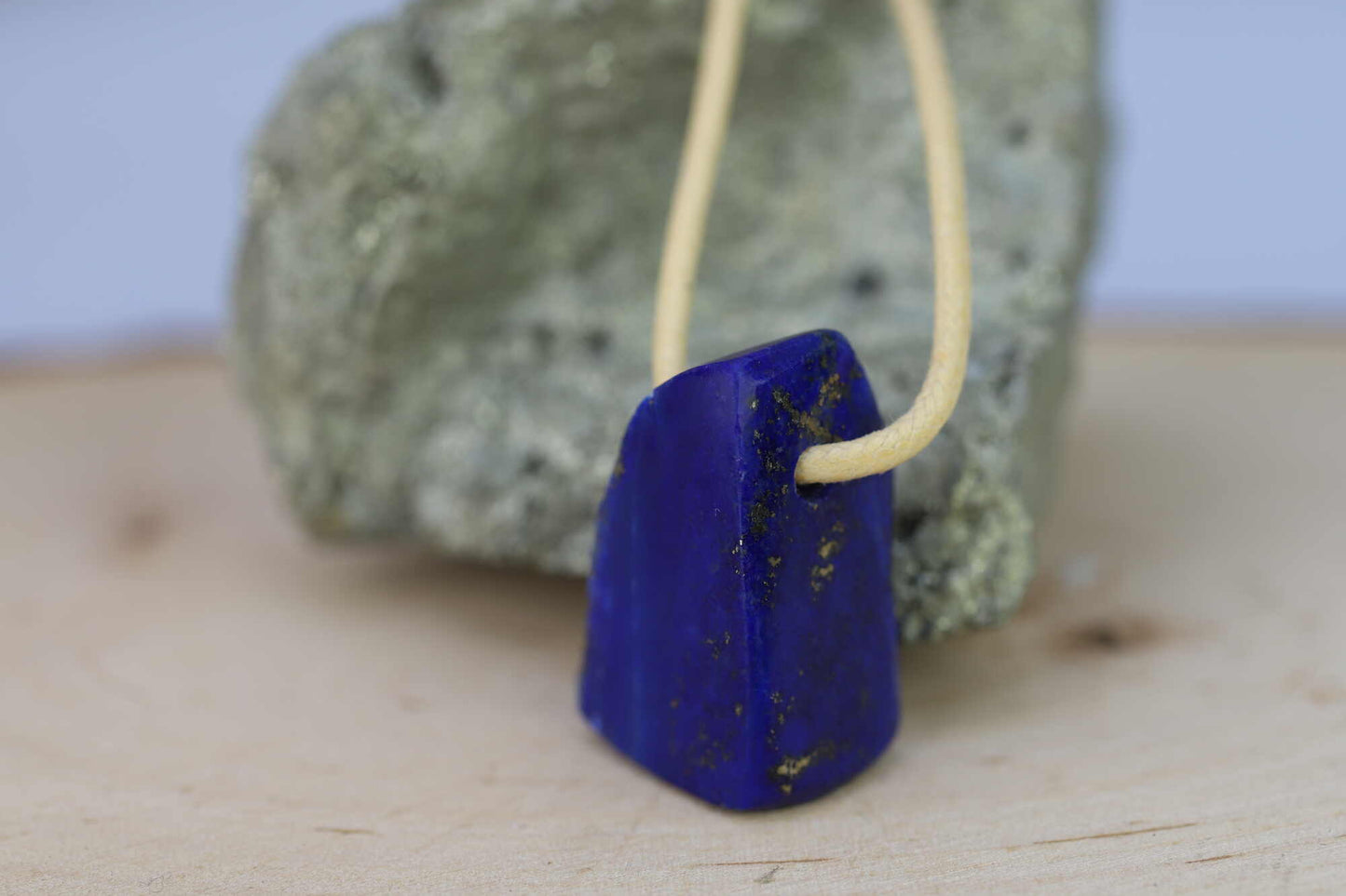 Kristallwerk präsentiert: Anhänger Lapis Lazuli auf goldenen Baumwollband aufgezogen und auf einem Pyritstein plaziert.