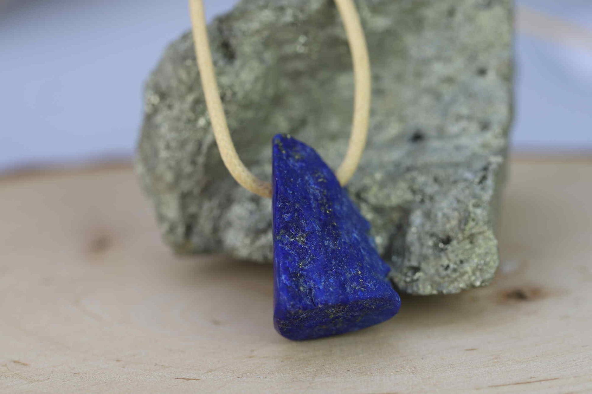 Kristallwerk präsentiert: Anhänger Lapis Lazuli auf goldenen Baumwollband aufgezogen und auf einem Pyritstein plaziert.