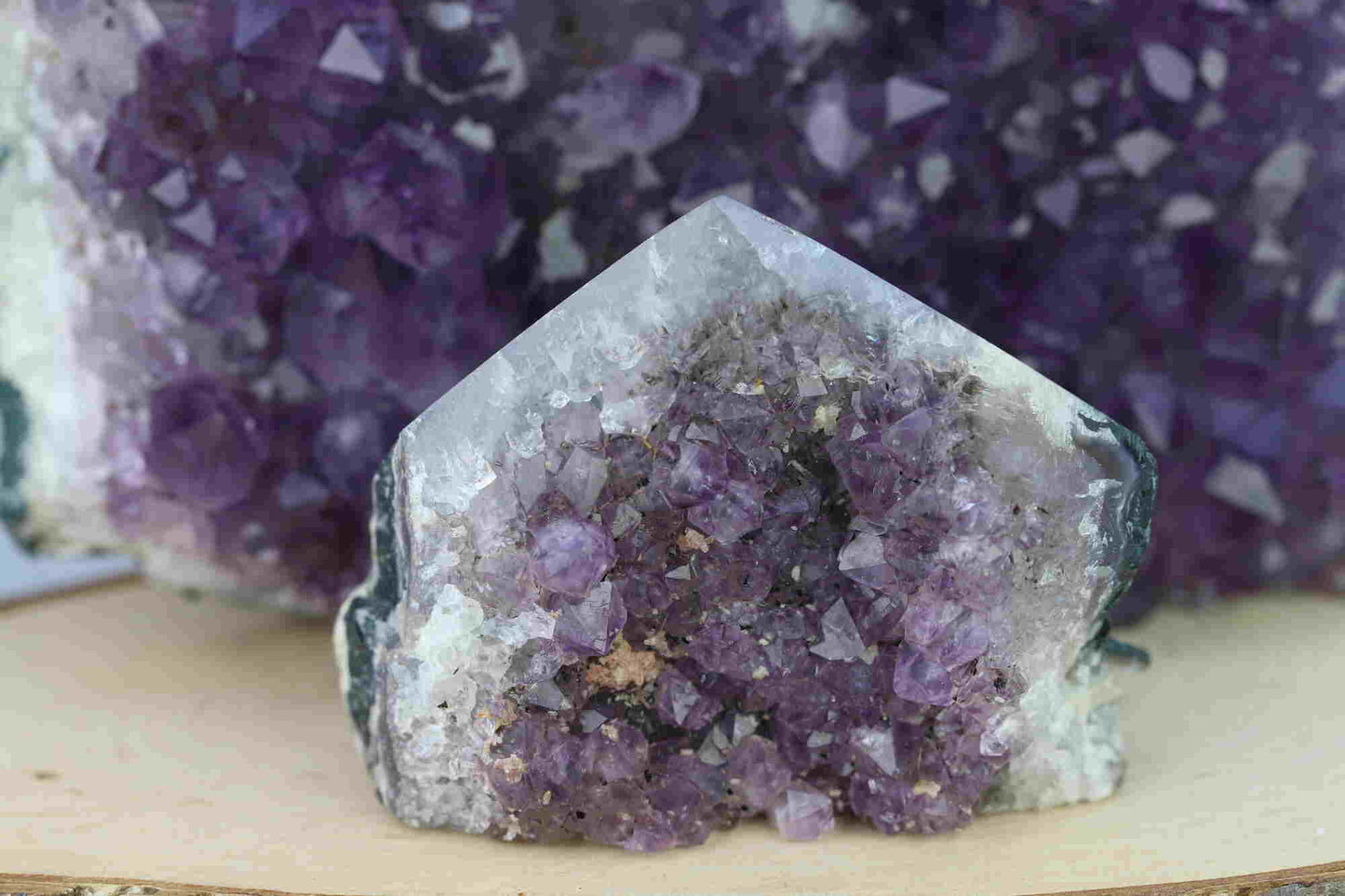 Kristallwerk präsentiert: Rohe Schätze Amethyst Spitze vor unscharfer Amethyststufe.