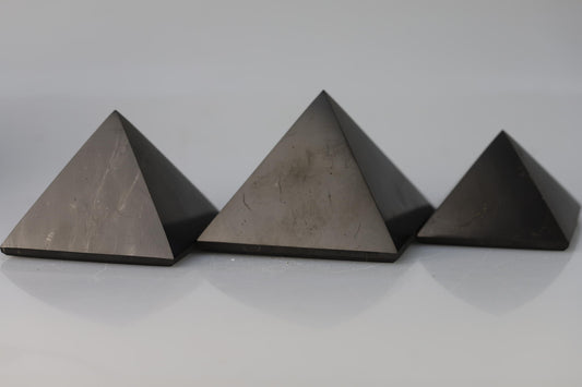 Kristallwerk präsentiert: Pyramide aus Schungit auf weiss glänzendem Untergrund.