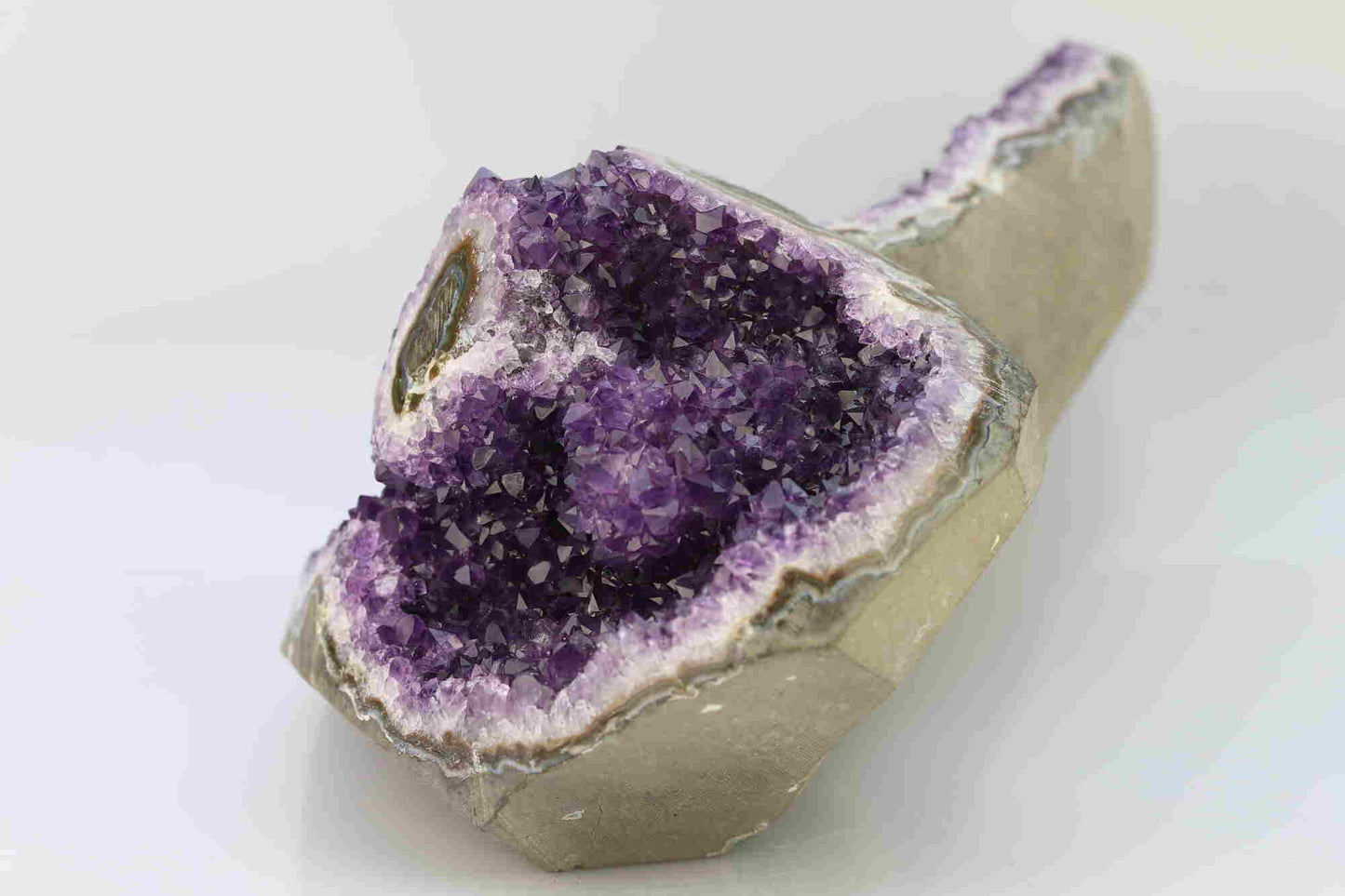 Kristallwerk präsentiert: Rohe Schätze Amethyst Herz Freeform Extra auf weiss glänzendem Untergrund.